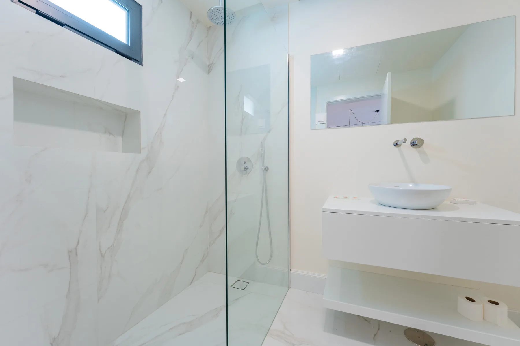 Un baño luminoso con una ducha de vidrio y un lavabo blanco.