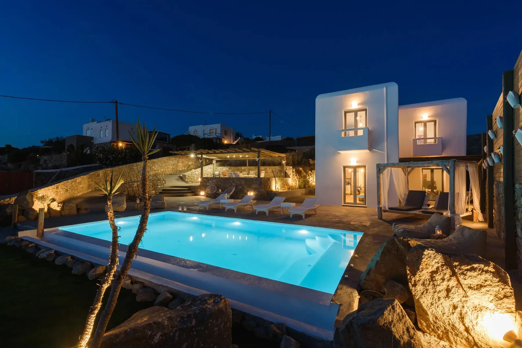An illuminated villa and swimming pool are visible at dusk.