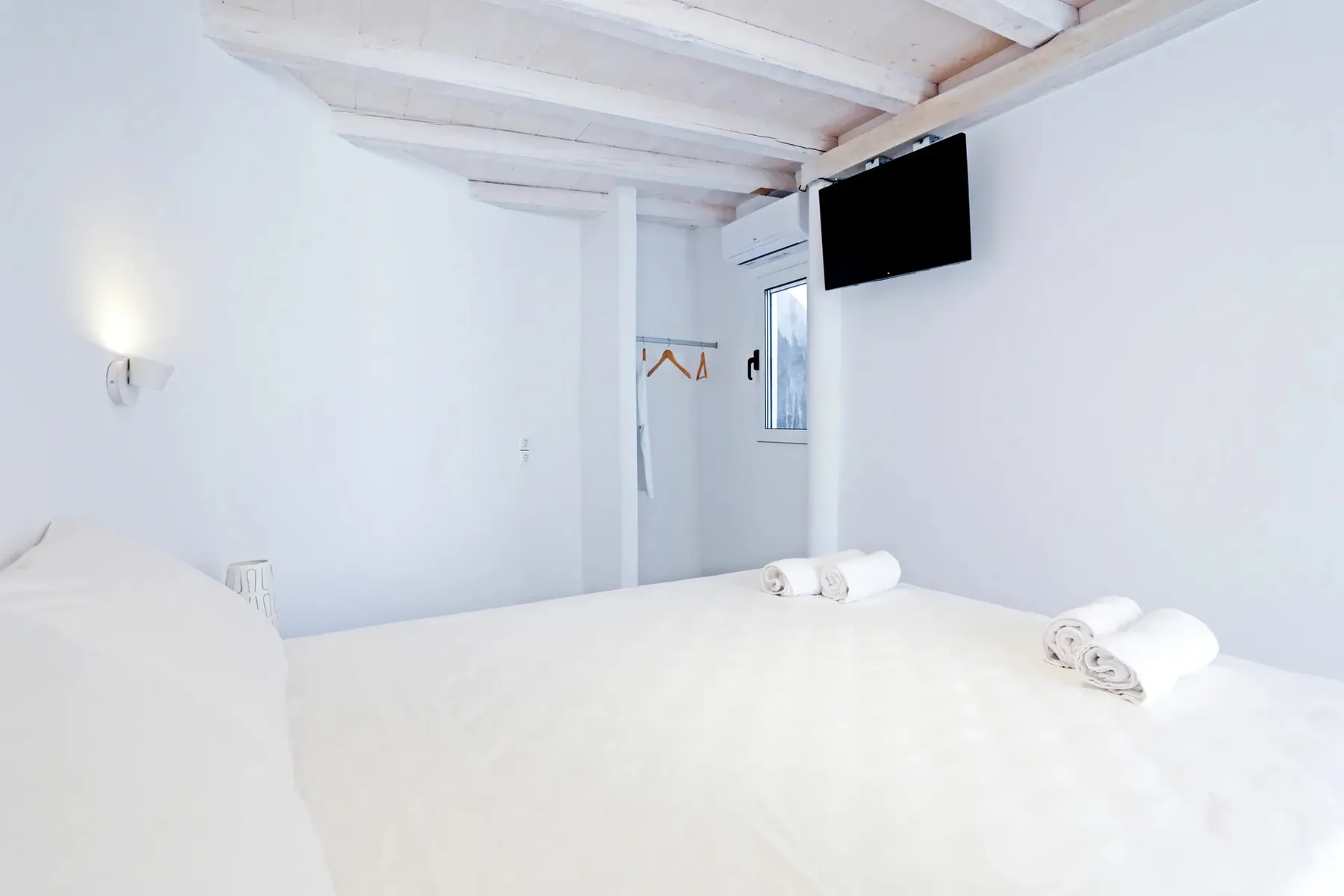 A bright bedroom with a white bed and a wall-mounted television.