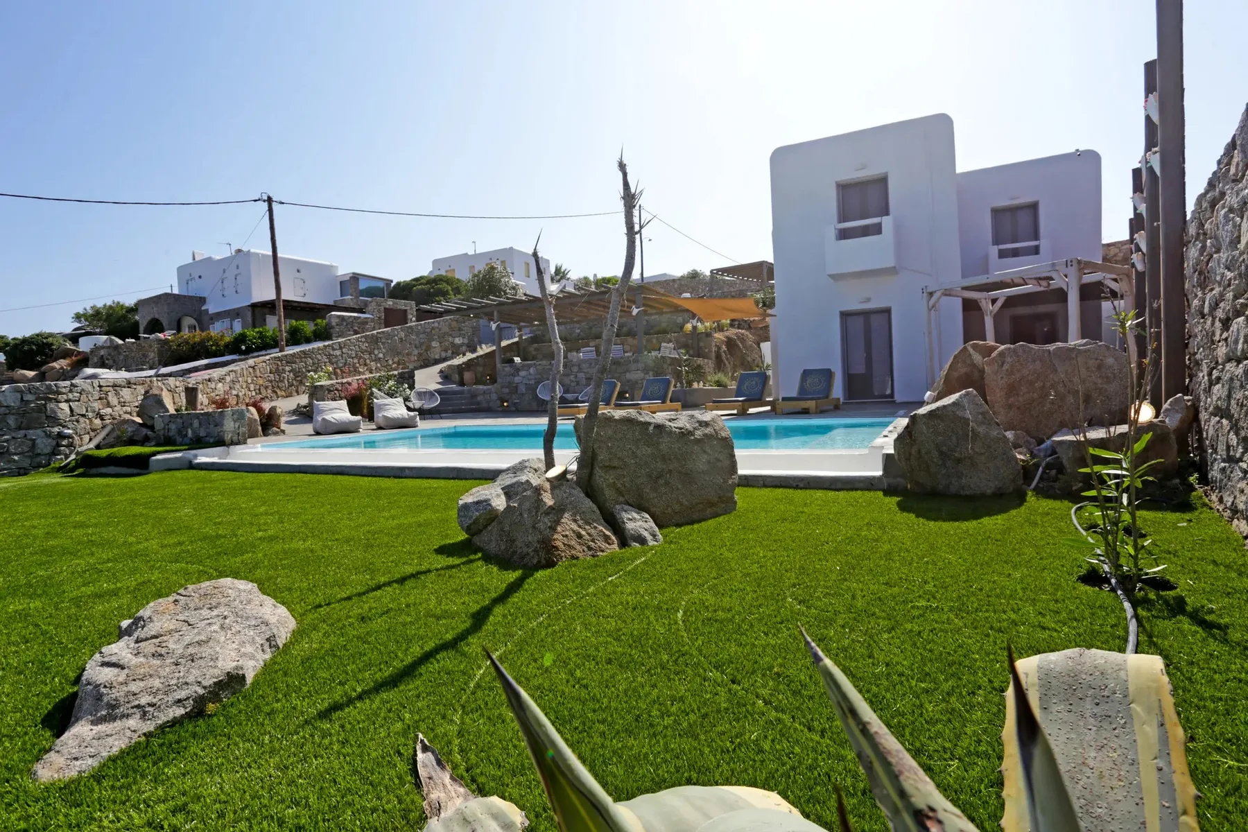 An outdoor swimming pool borders a green lawn with scattered rocks.