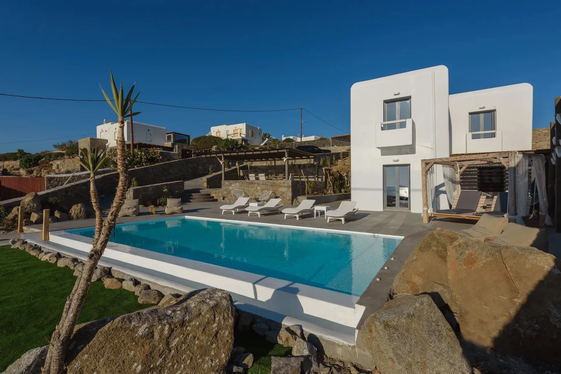 A swimming pool beside a modern white building and outdoor loungers.