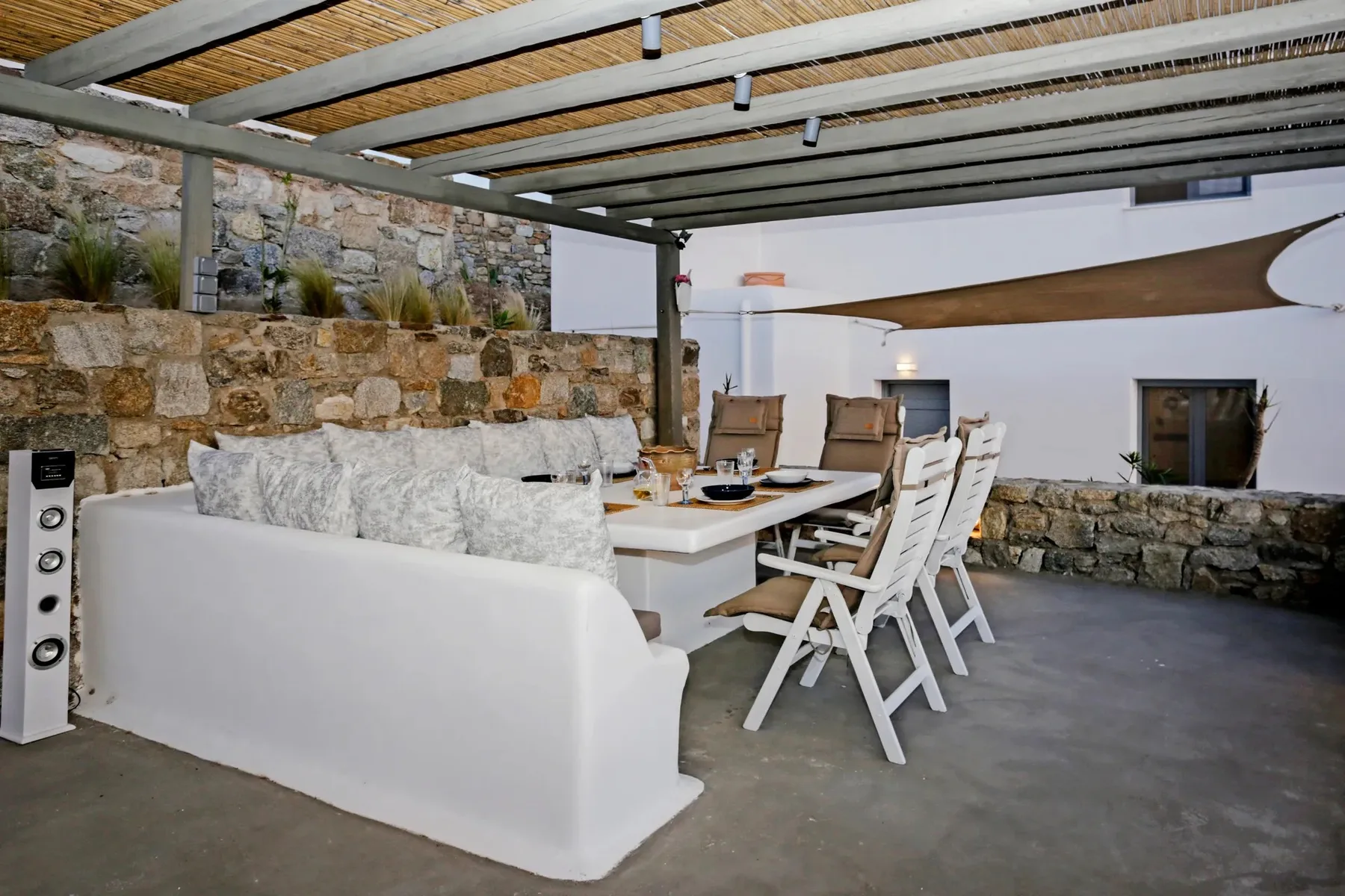 A covered patio seating and dining area with a long table and white chairs.