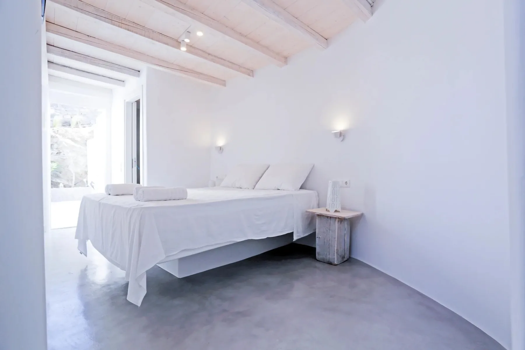 A bright bedroom with a white bed and exposed ceiling beams.