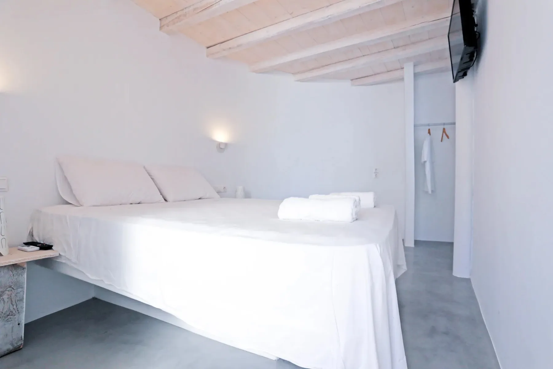 A bright bedroom with white bedding and exposed ceiling beams.