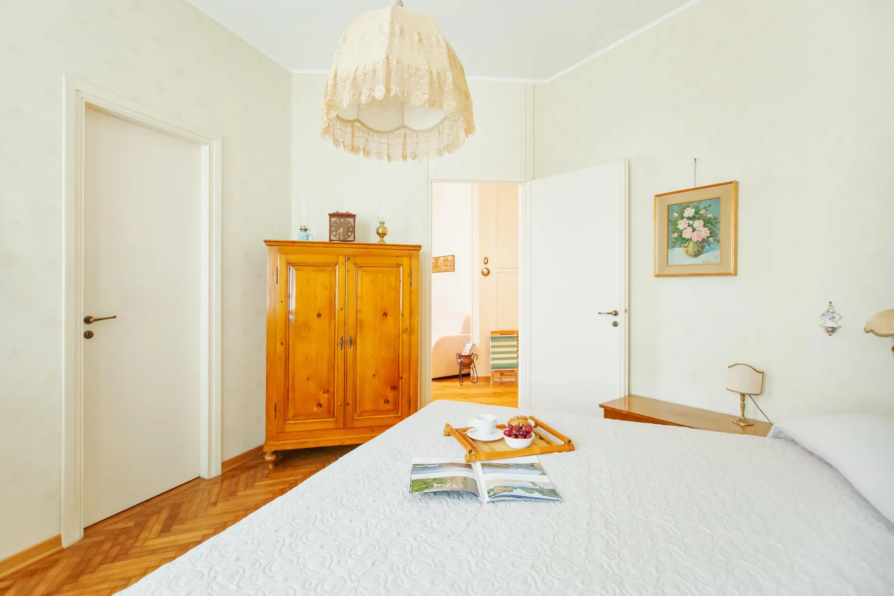 A bright bedroom with a wooden wardrobe and a bed covered in white bedding.