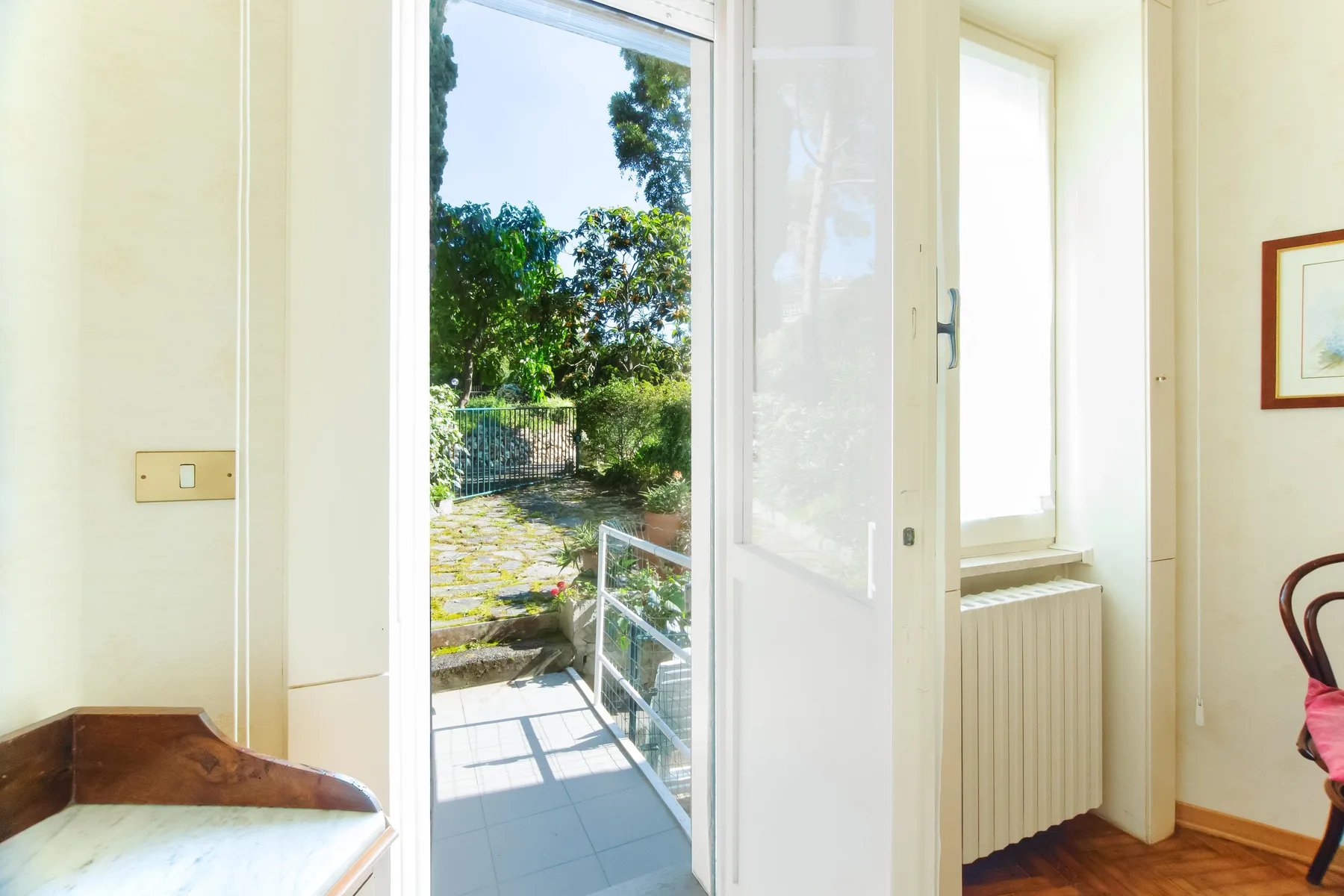 A bright room opens onto a garden patio through a glass door.