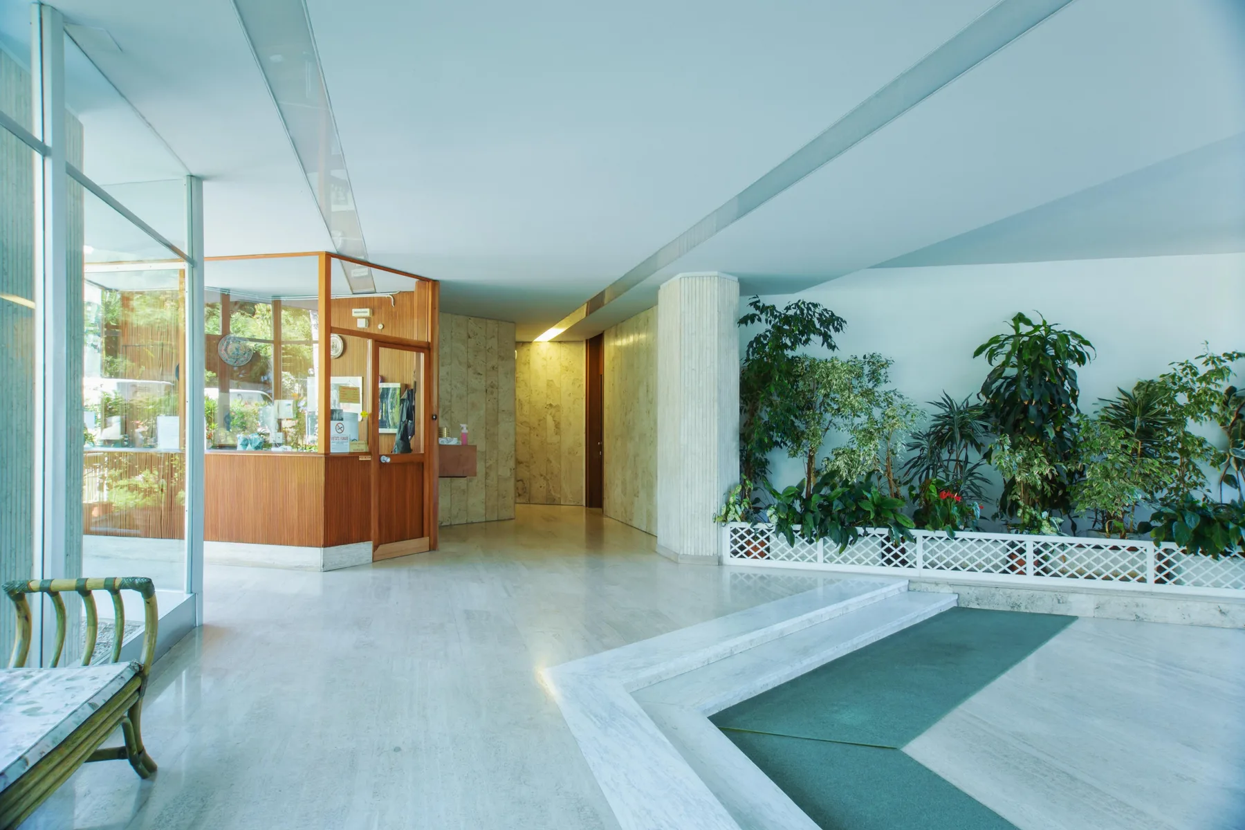 An indoor pool area with a glass-fronted wooden counter and plants.