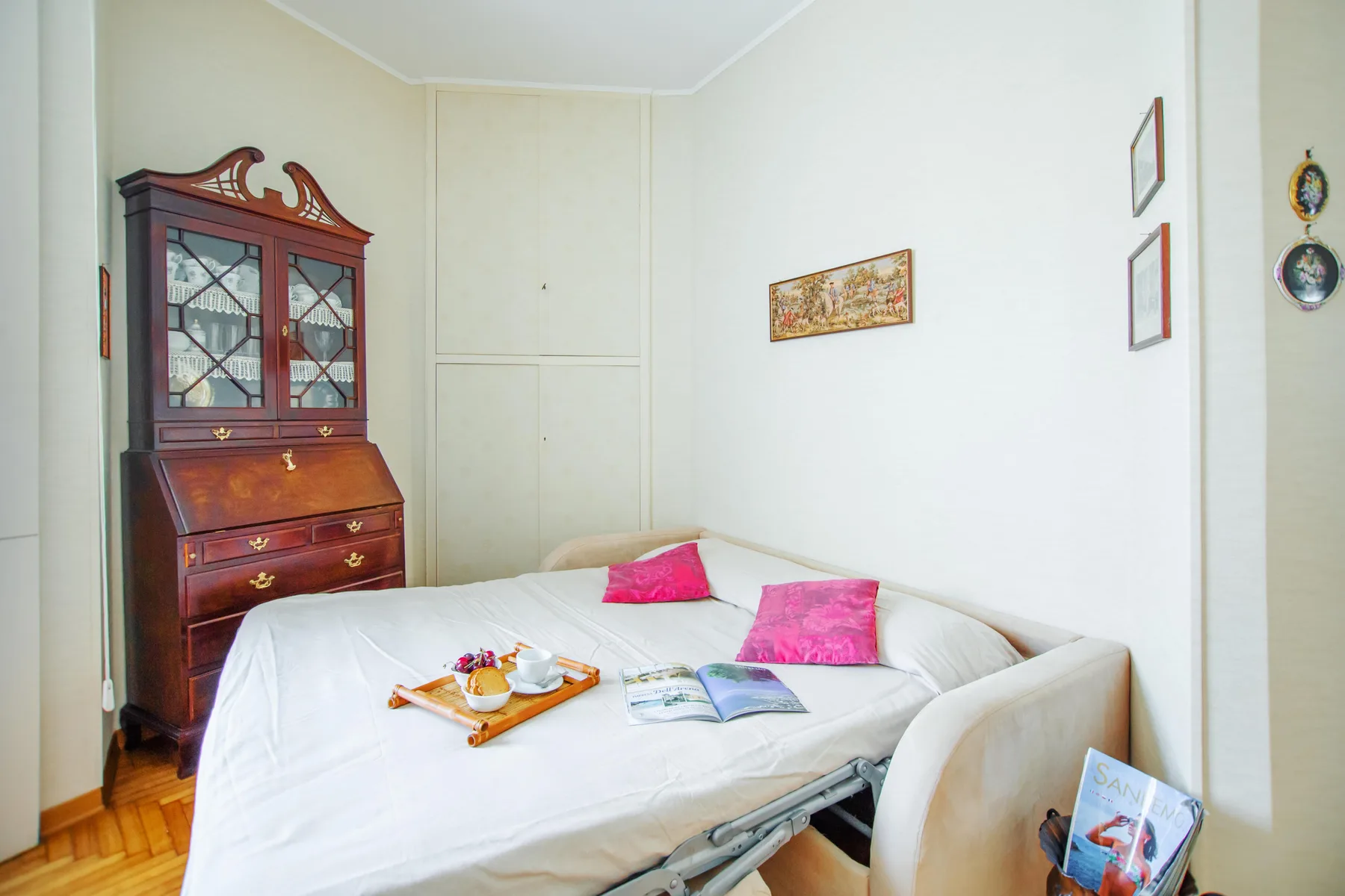A bright bedroom with a bed, pink cushions, and a wooden cabinet.
