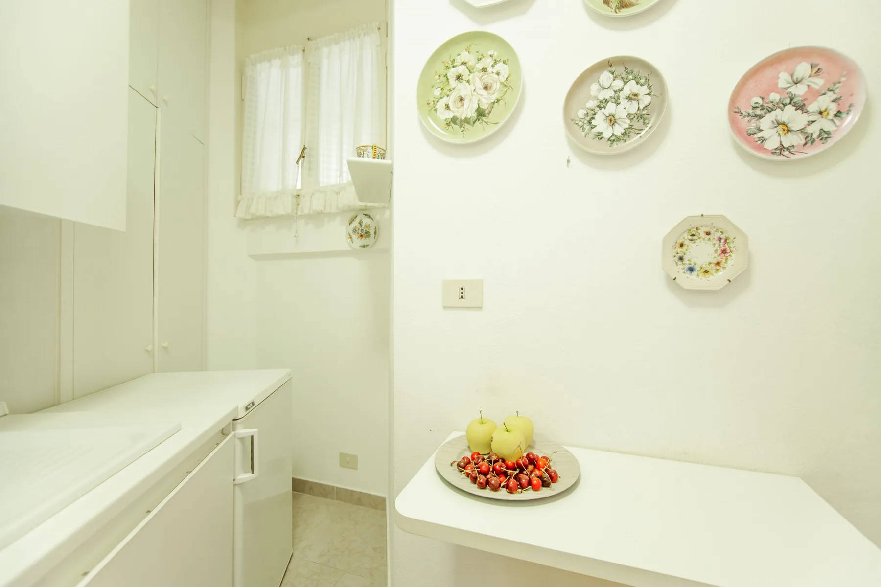 A bright kitchen with white countertops and decorative plates on the wall.