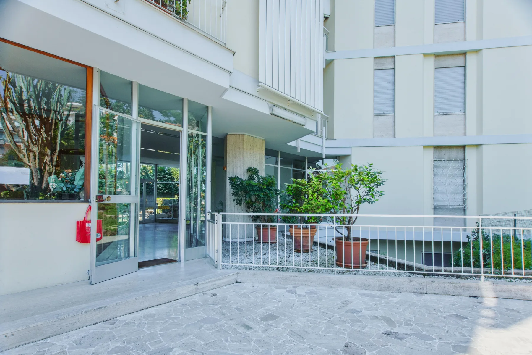 A building entrance opens onto a paved courtyard with potted plants.