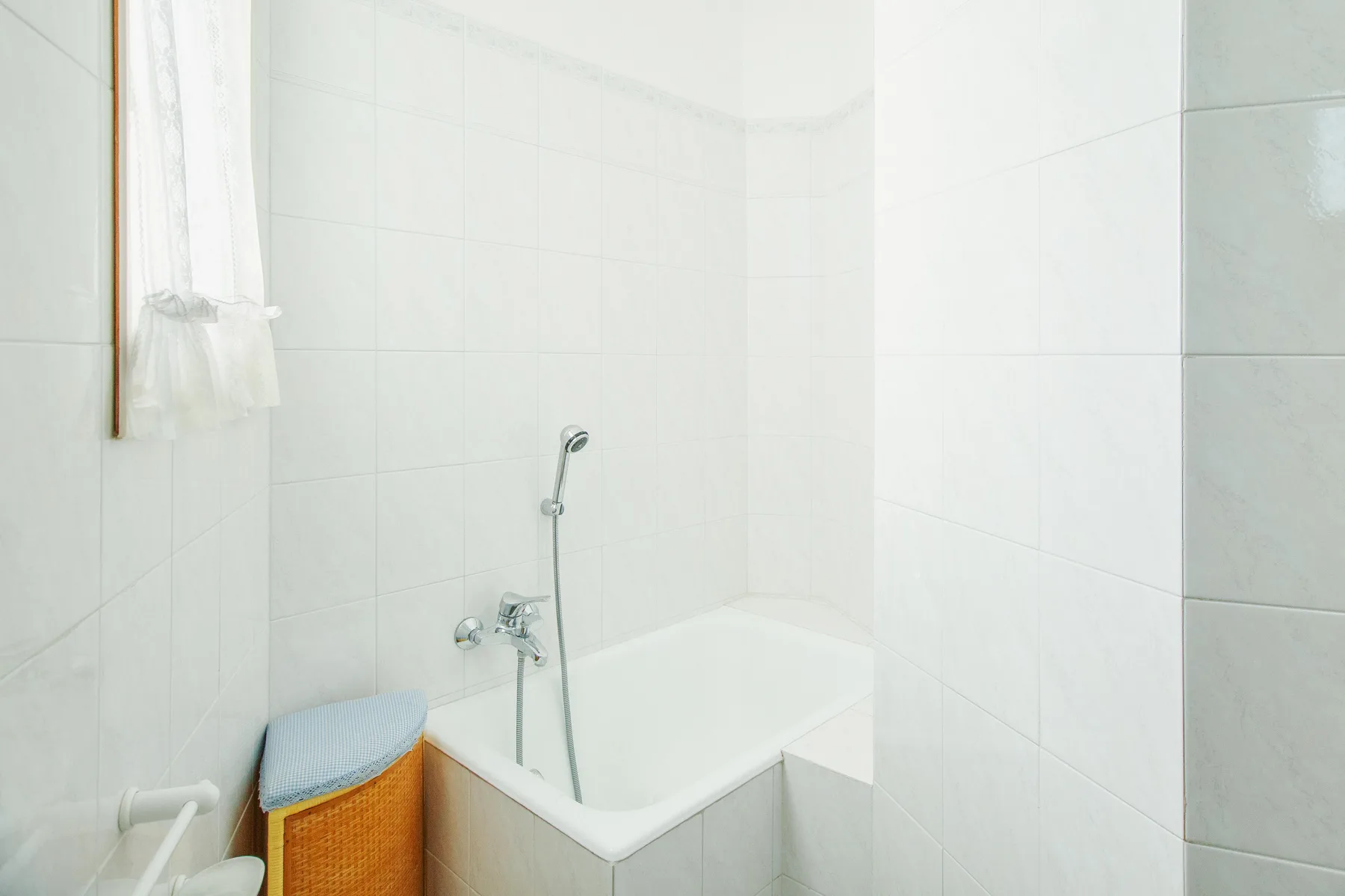 A tiled bathroom with a bathtub and handheld shower.