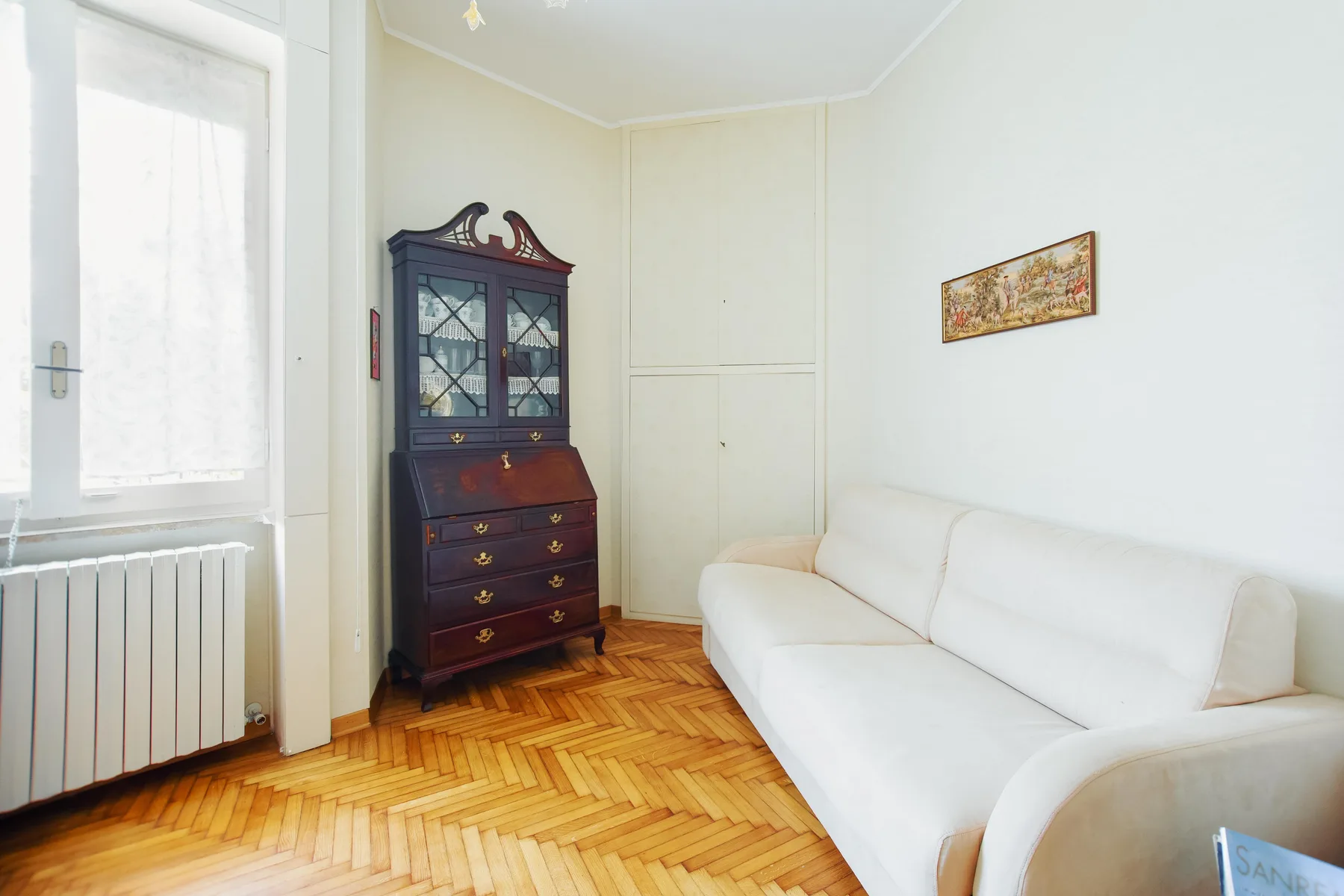 A bright living room with white seating and a dark wooden cabinet.