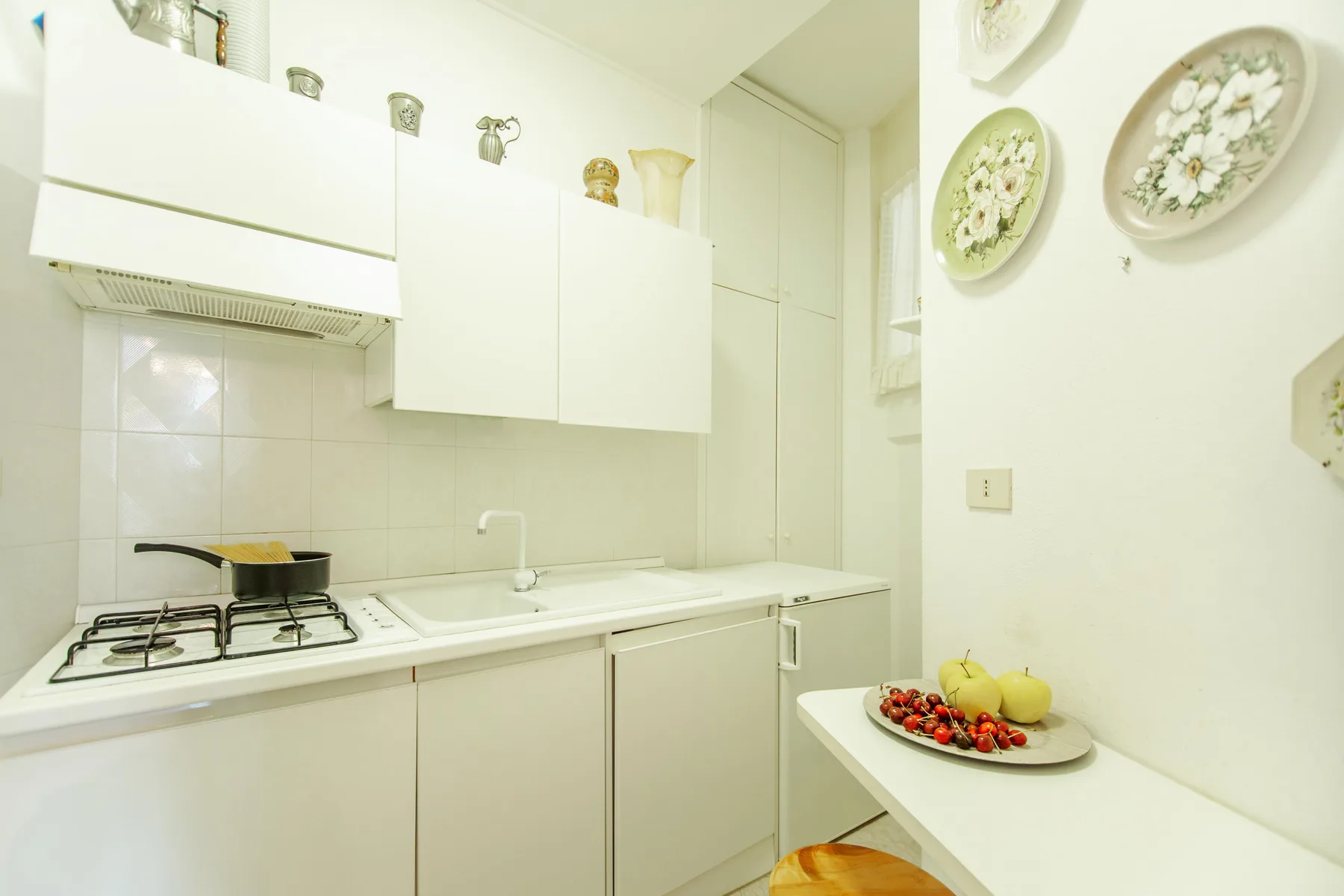 A bright kitchen with a stovetop, sink, and fruit on the counter.