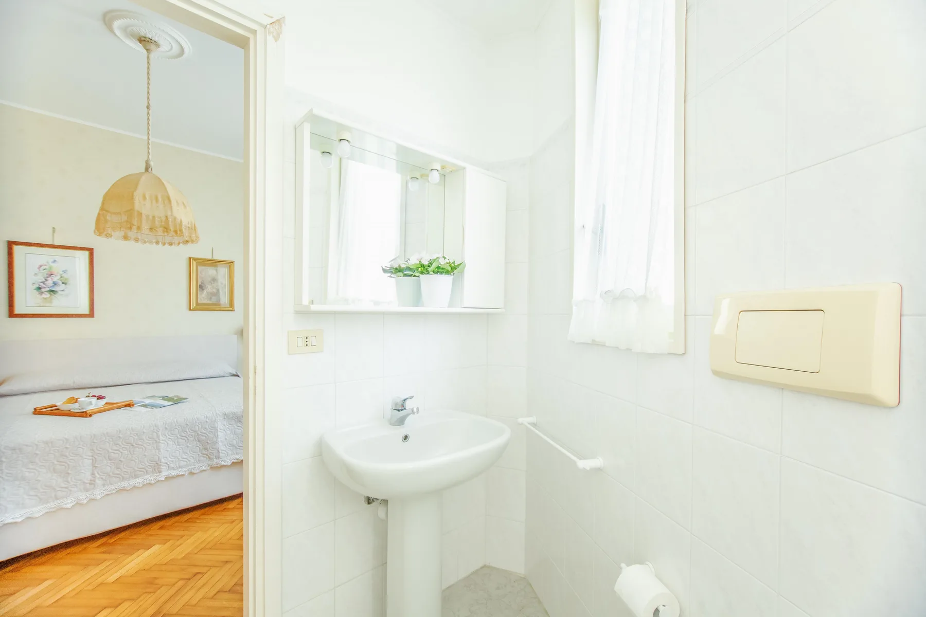 A bright bathroom with a pedestal sink and a view into the adjoining bedroom.
