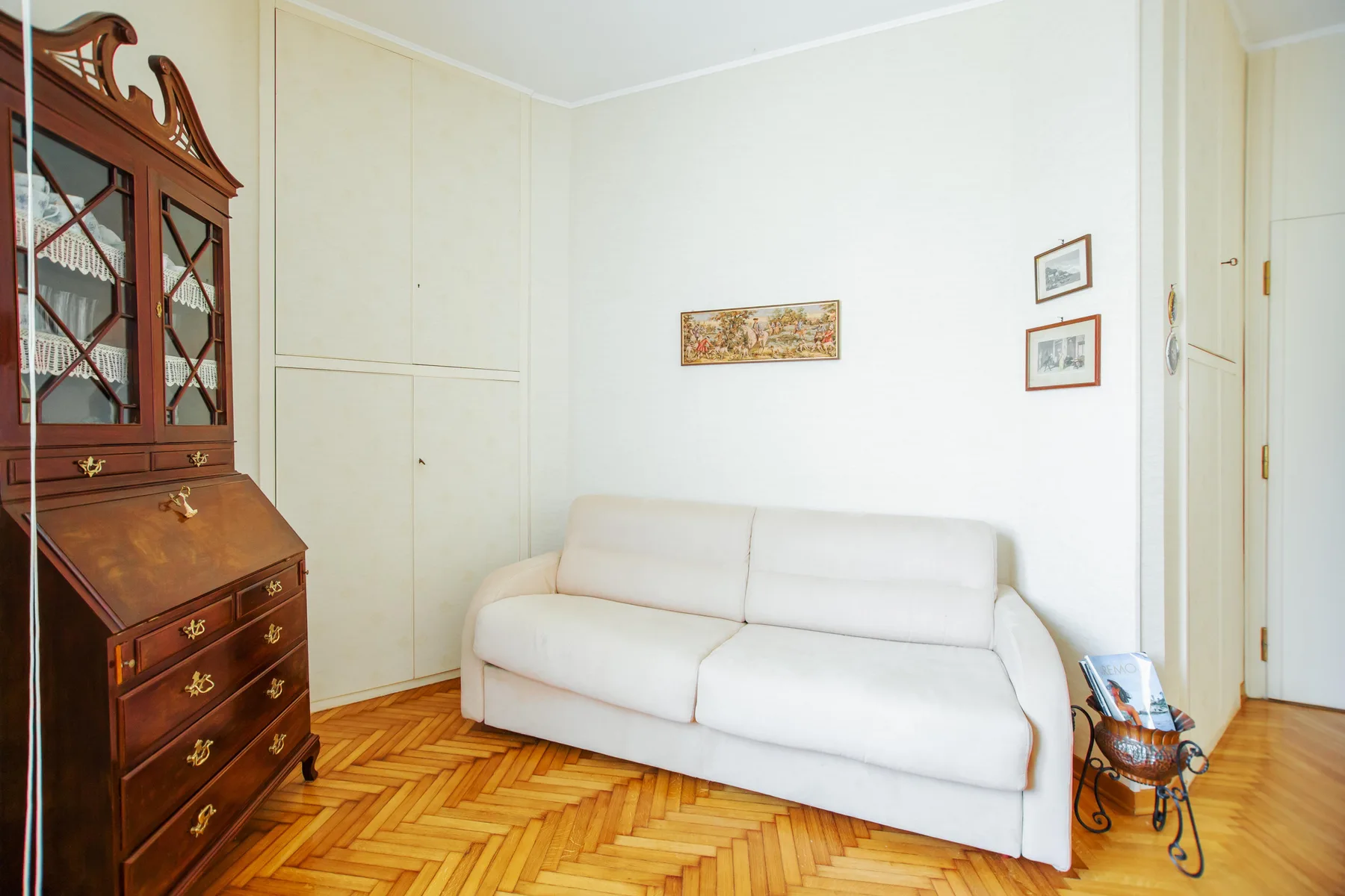 A bright sitting room with a white sofa and wooden display cabinet.