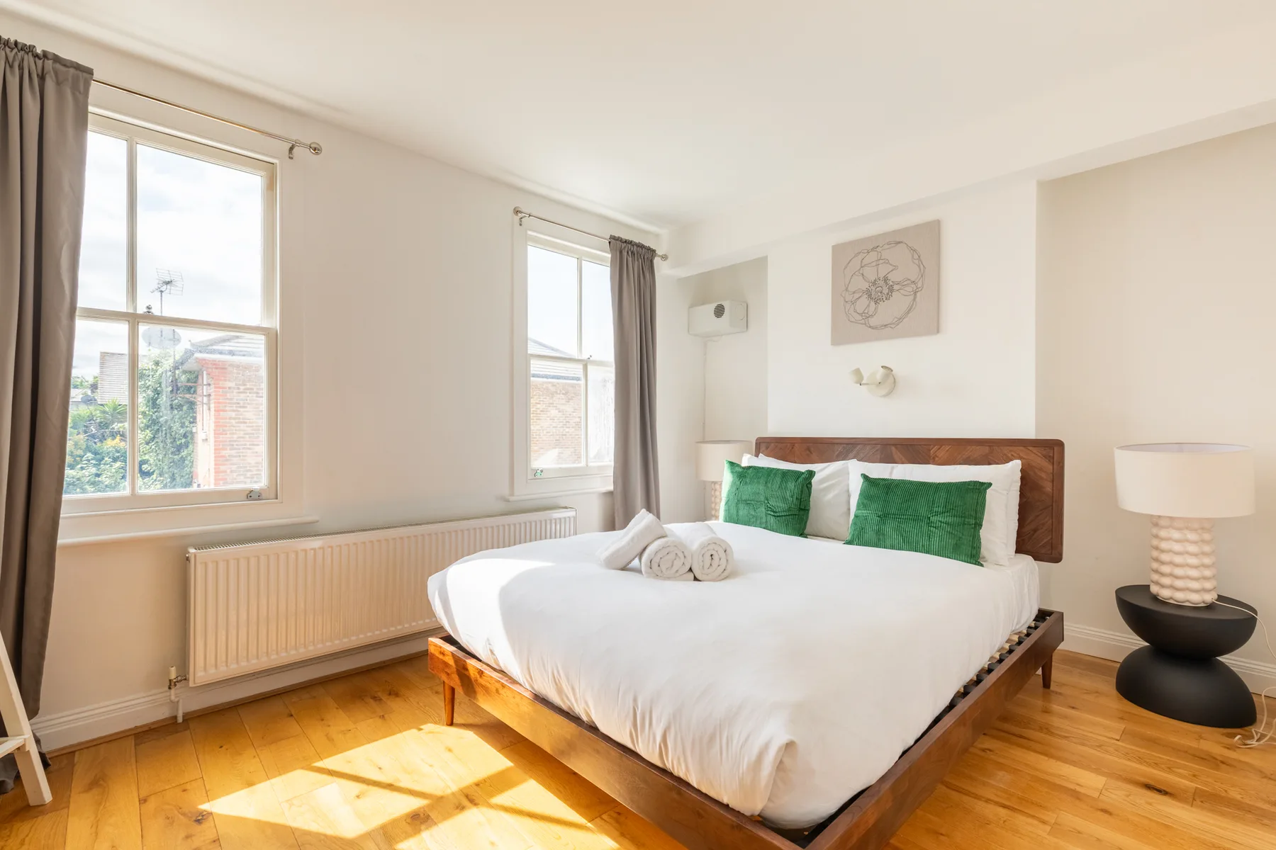 Un dormitorio luminoso tiene una cama de madera con ropa de cama blanca y almohadas verdes.