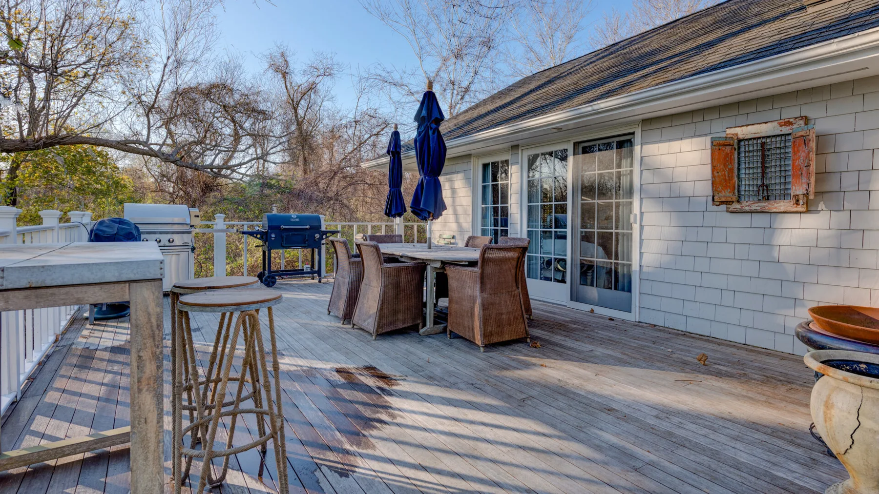 Una terraza exterior junto a una casa tiene una mesa de comedor y asientos.