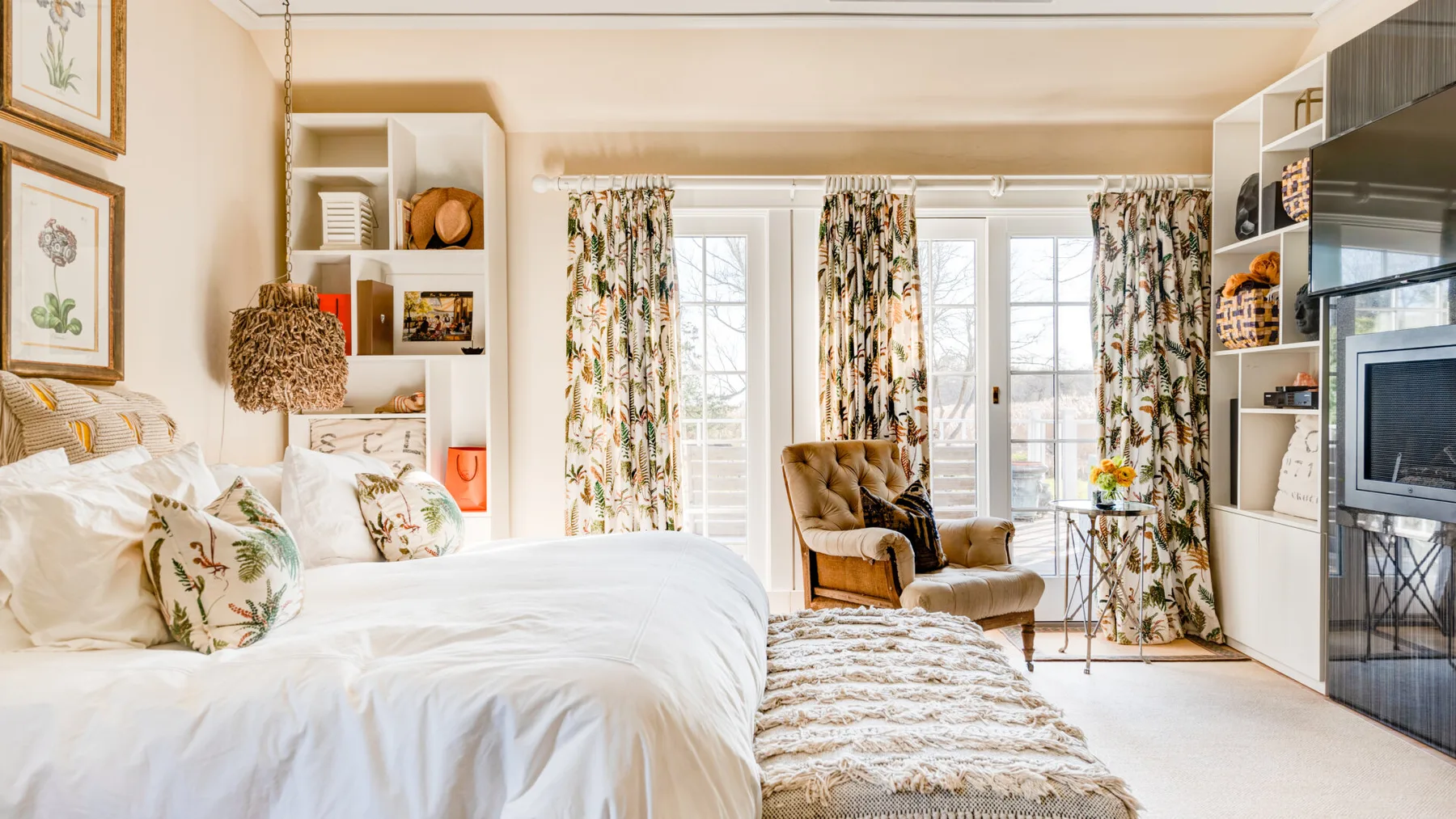 Un dormitorio luminoso con una cama grande, cortinas estampadas y una zona de estar junto a las ventanas.