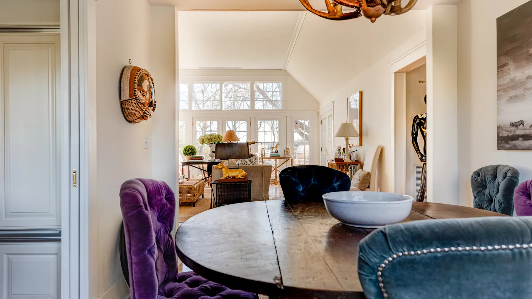 Una sala luminosa con una mesa redonda de madera y asientos junto a grandes ventanas.