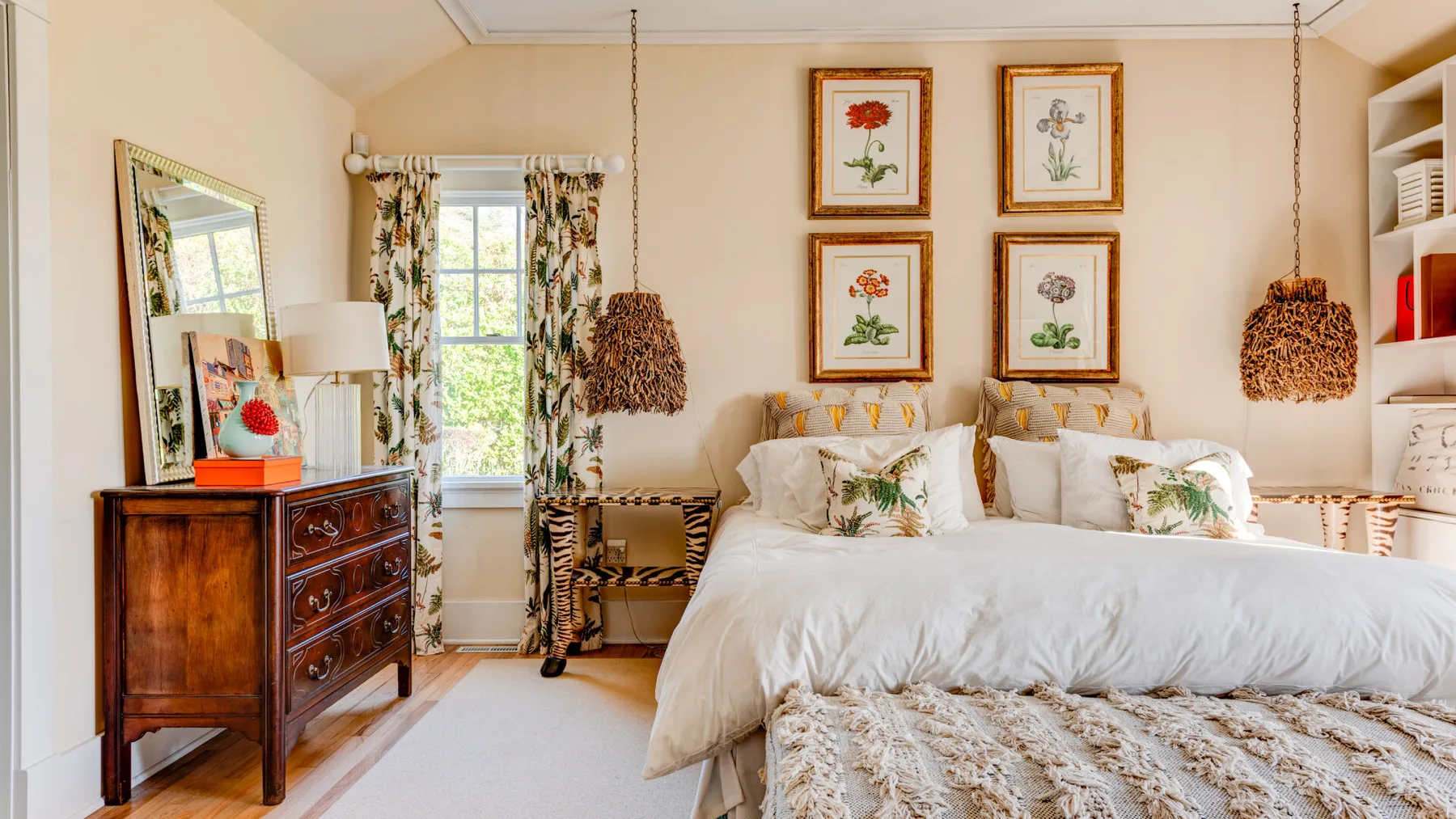 Un dormitorio luminoso con una cama grande, cortinas florales y láminas botánicas enmarcadas.