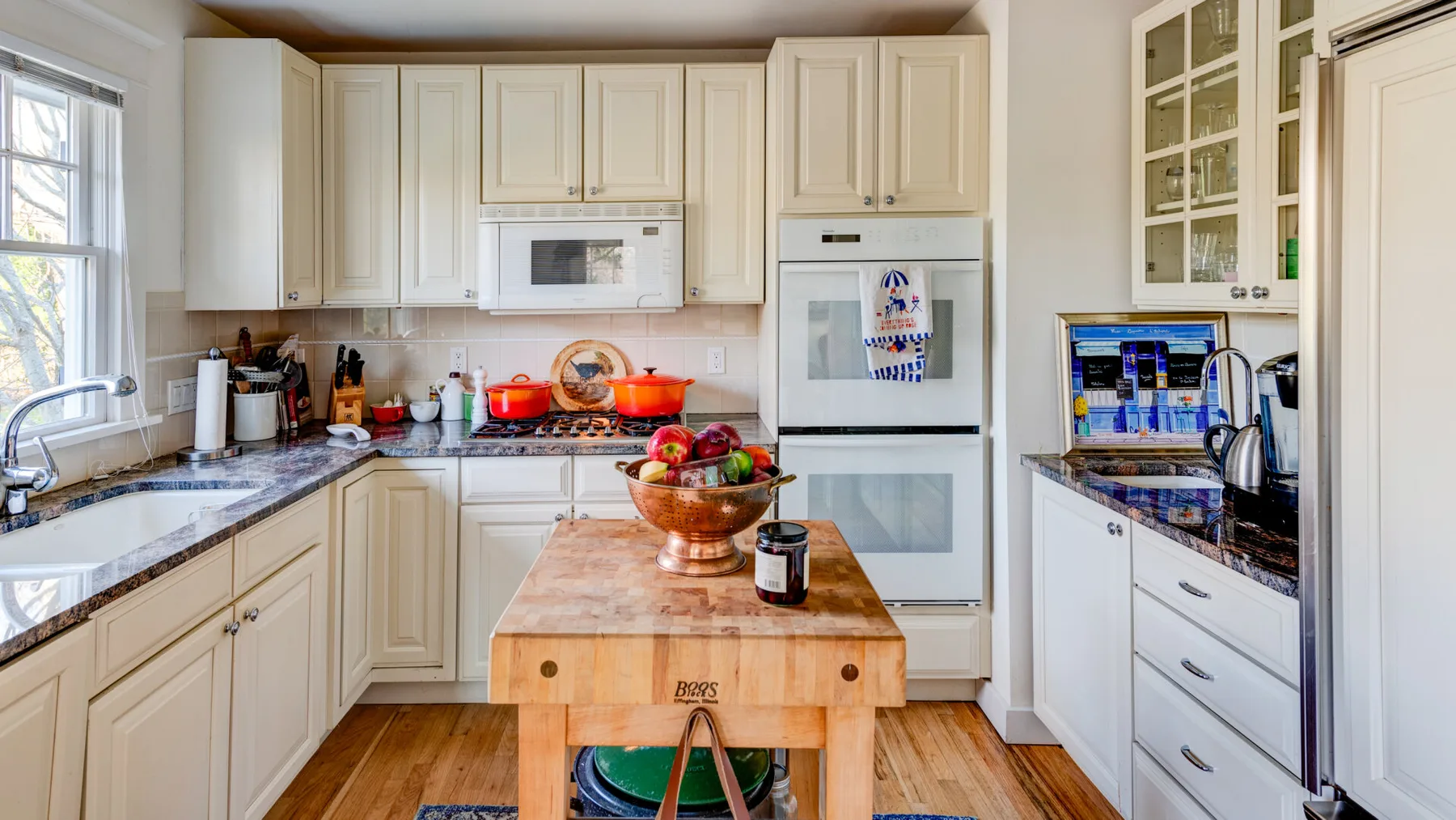 Una cocina luminosa con gabinetes color crema, encimeras oscuras y una mesa de trabajo de madera.