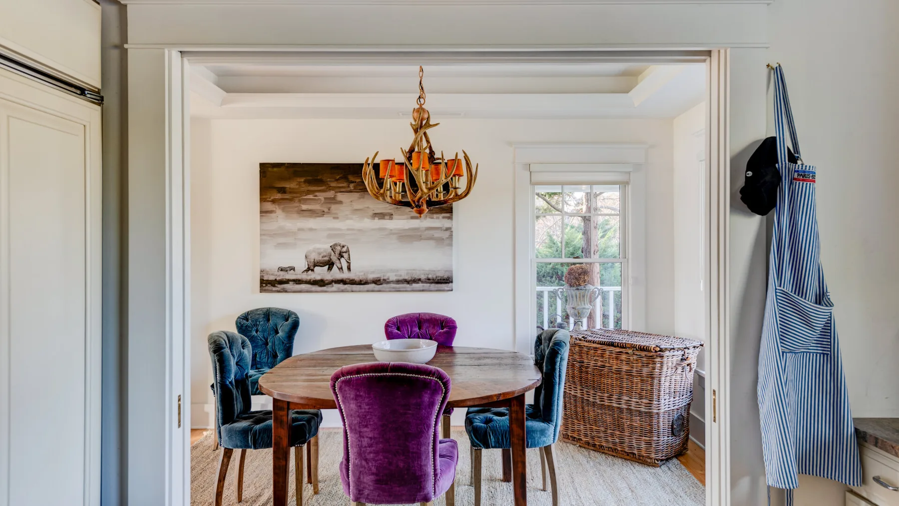 Un comedor con una mesa redonda, asientos coloridos y una cesta tejida junto a la ventana.