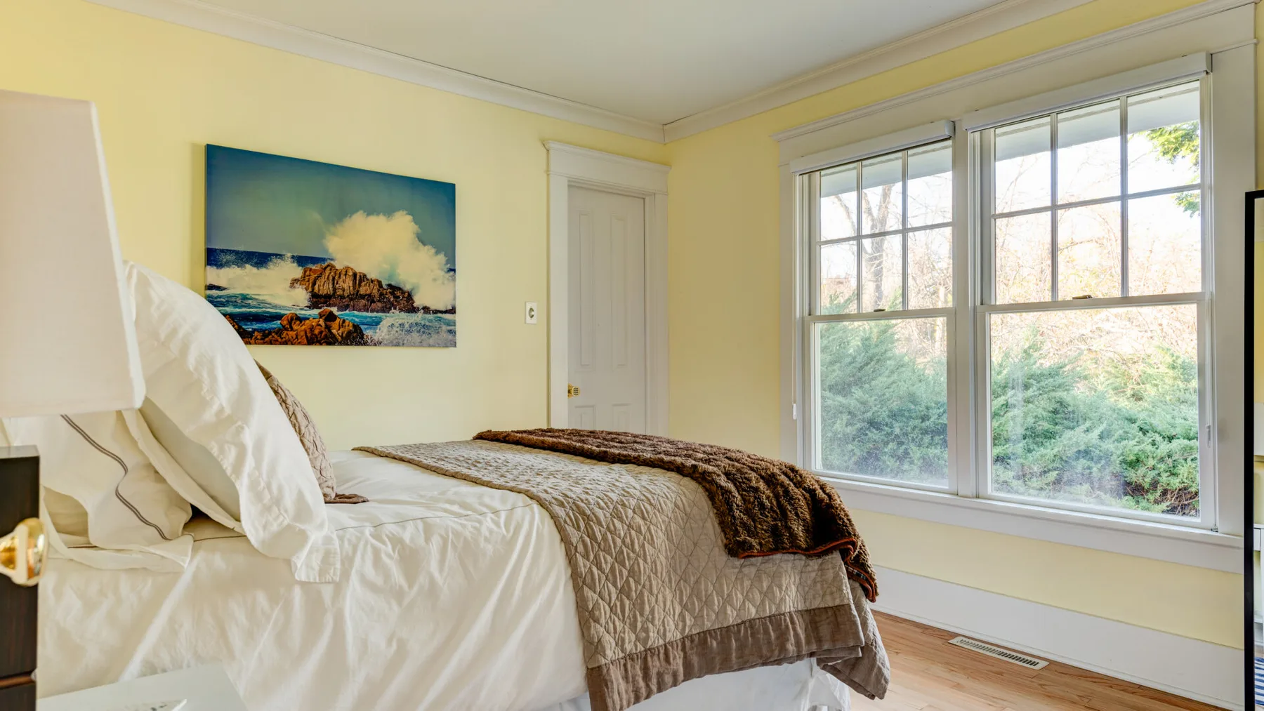 Un dormitorio luminoso con una cama junto a grandes ventanas que dan a la vegetación.