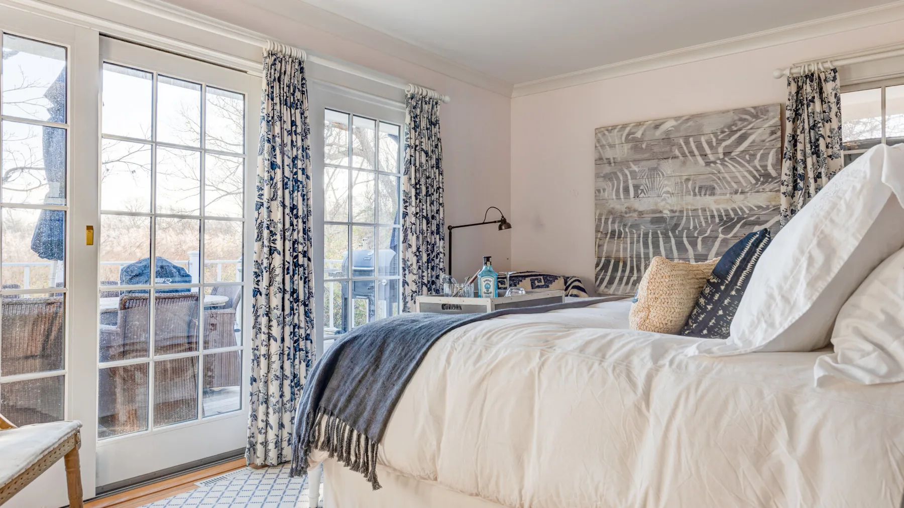 Un dormitorio luminoso con una cama junto a ventanas altas y puertas de vidrio.