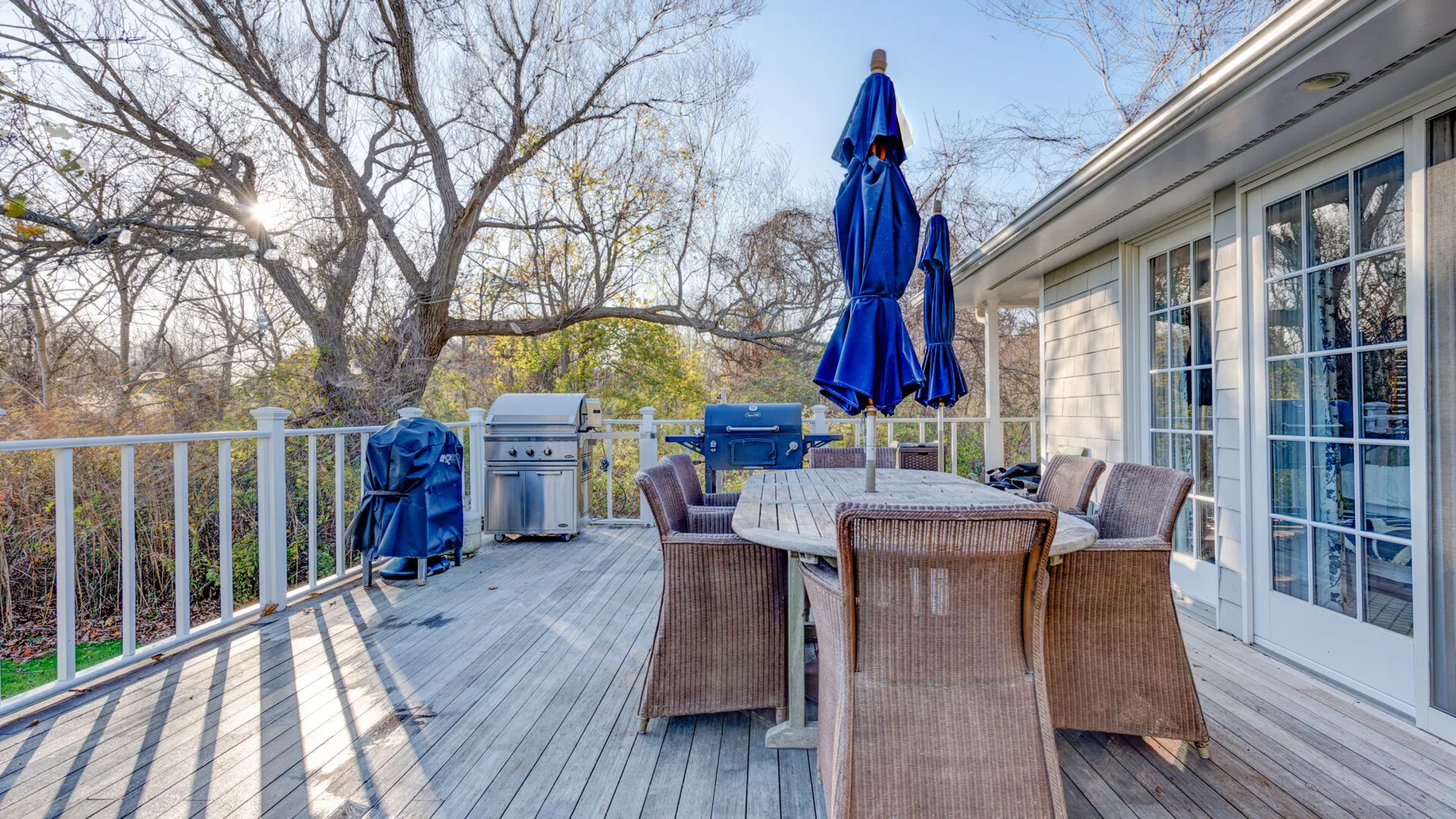 Una terraza exterior amueblada con mesa de comedor, asientos y sombrillas azules cerradas.