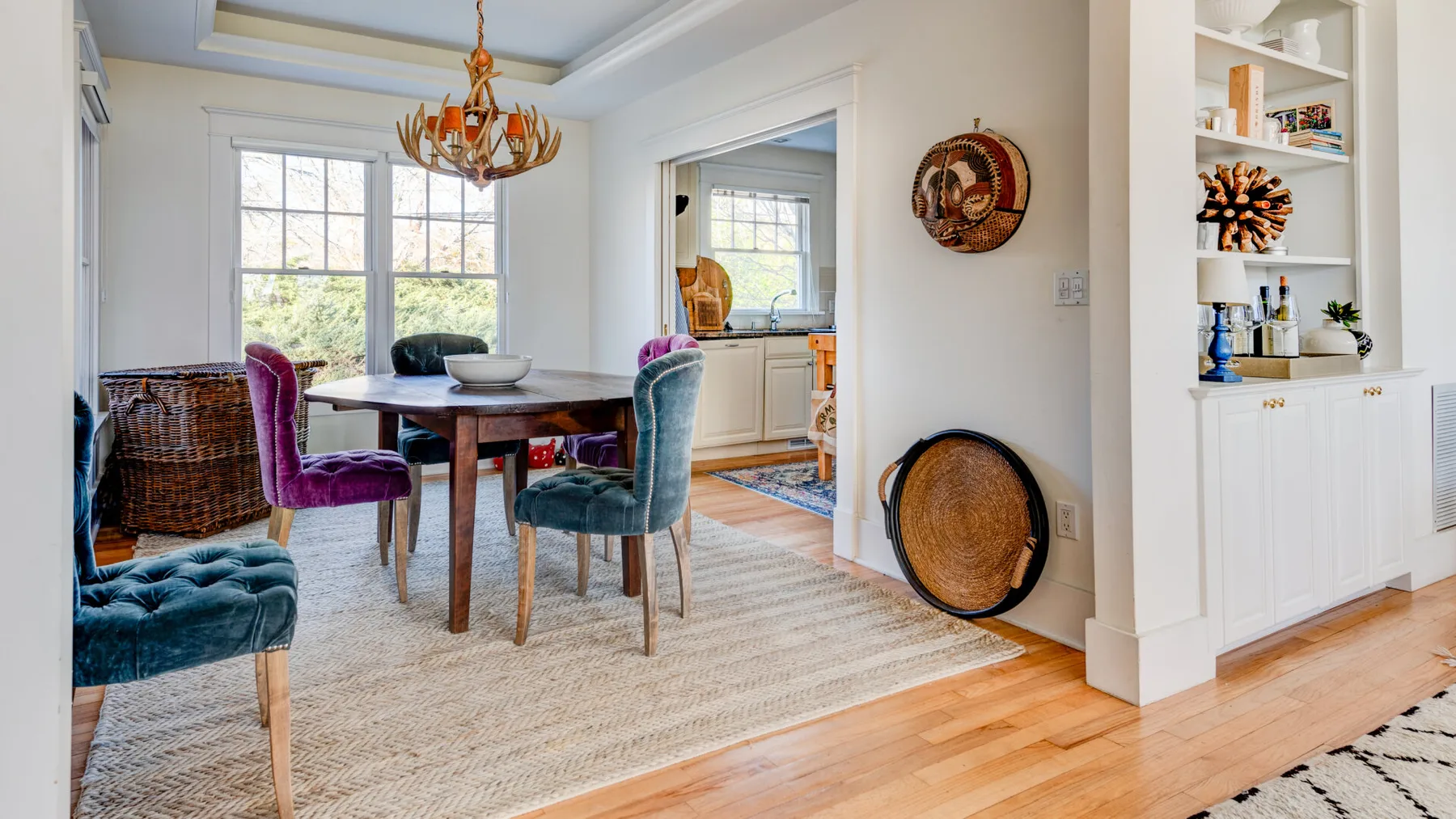Comedor con una mesa de madera y asientos tapizados de colores.