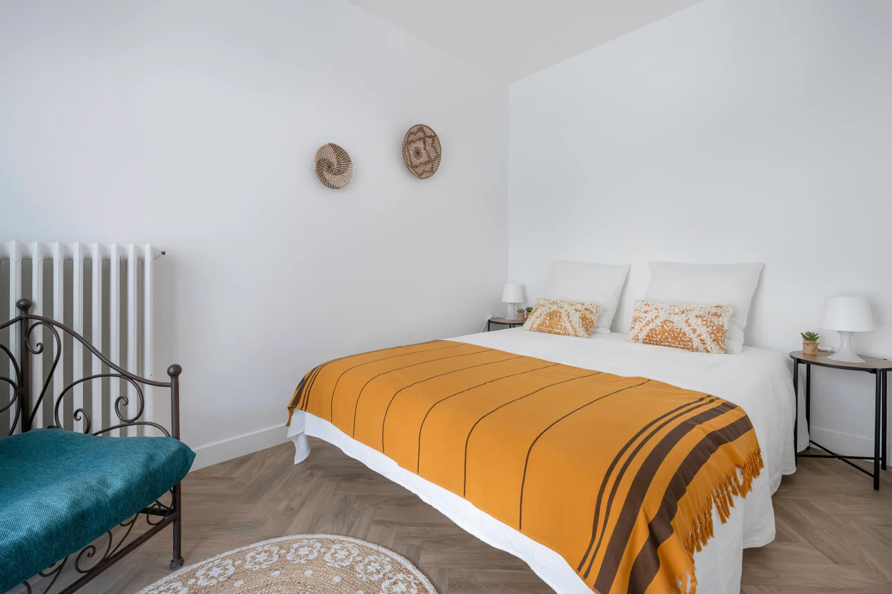 Un dormitorio luminoso con una cama cubierta por una manta naranja a rayas.