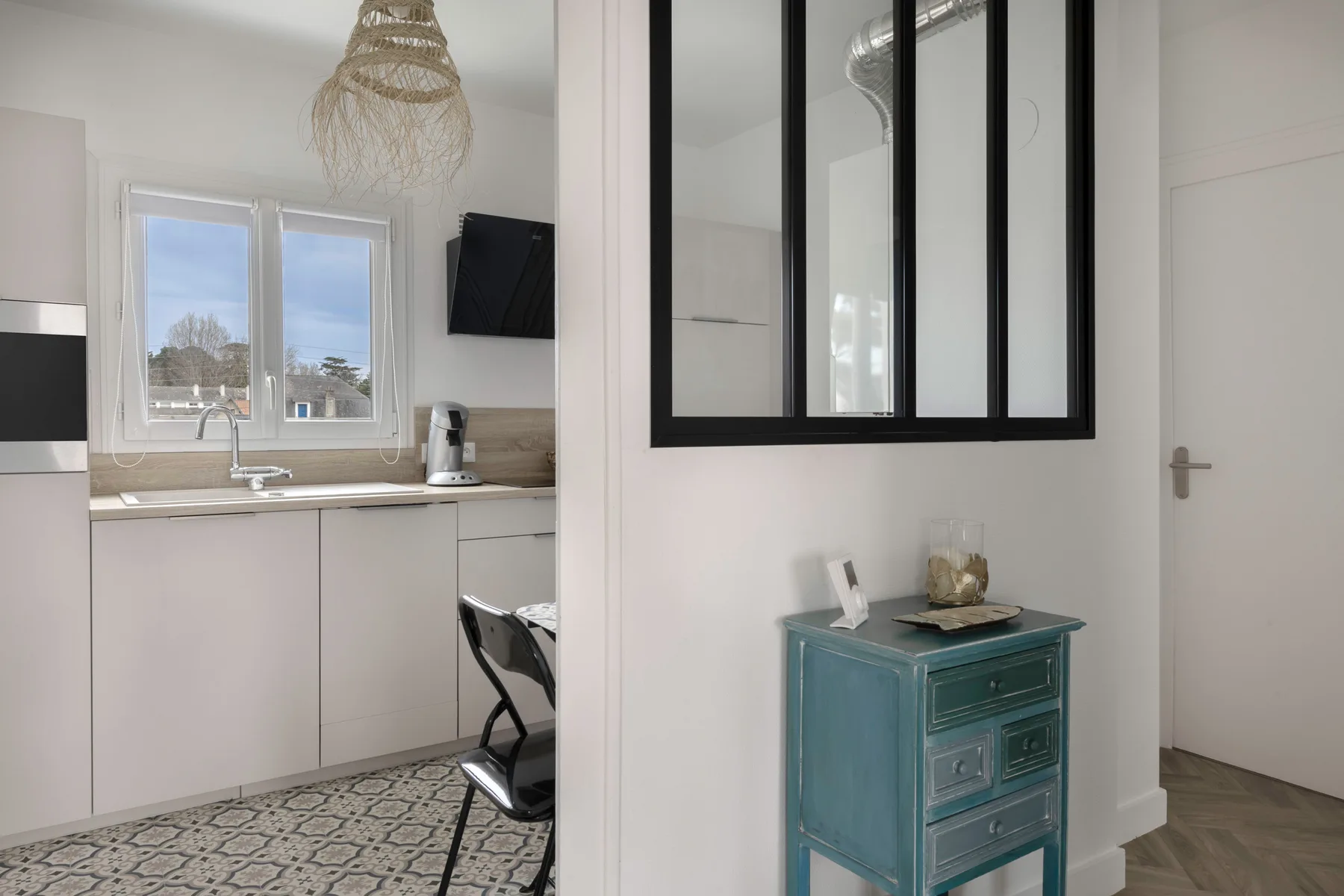 Una cocina luminosa se abre a un pasillo con un pequeño mueble verde azulado.