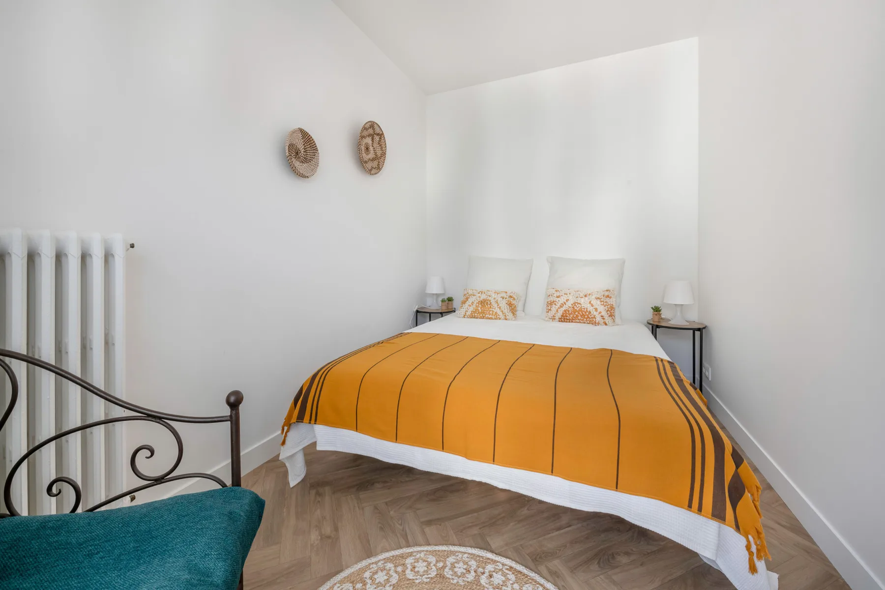 Un dormitorio con una colcha naranja y paredes blancas.