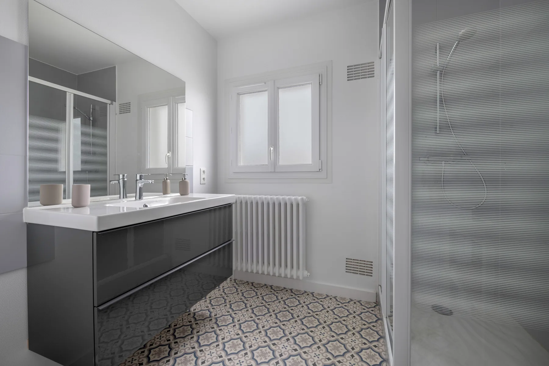 Un baño luminoso con lavabo doble y suelo estampado.