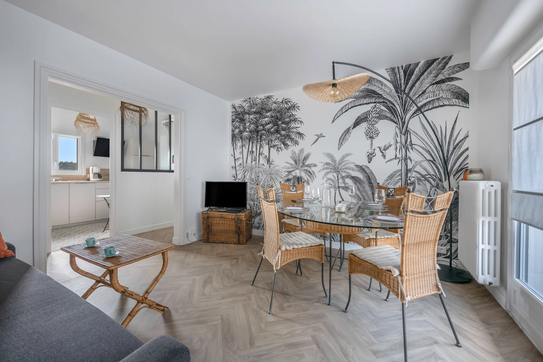Sala de estar y comedor con asientos de mimbre y un mural botánico.