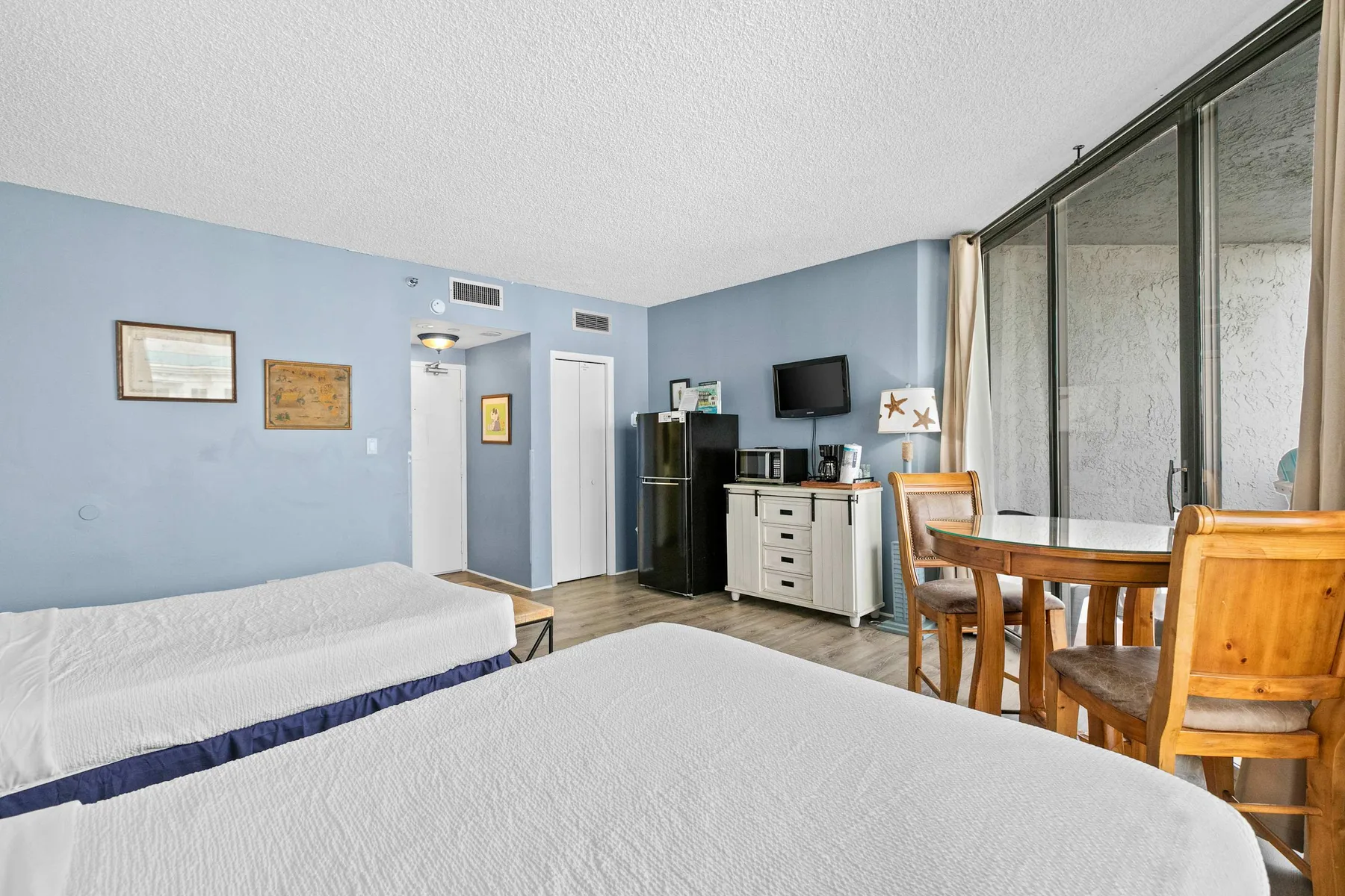 A bedroom with two beds, a dining table, and a kitchenette along the far wall.