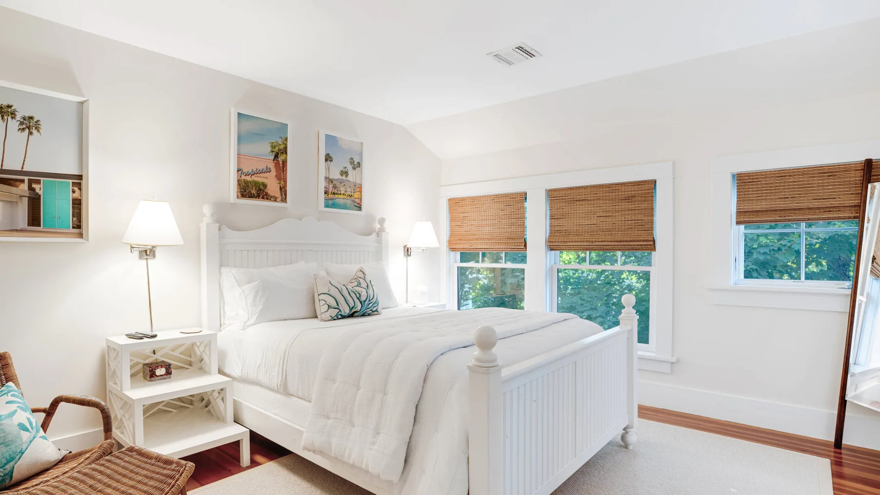 A bright bedroom with a white bed and windows overlooking greenery.
