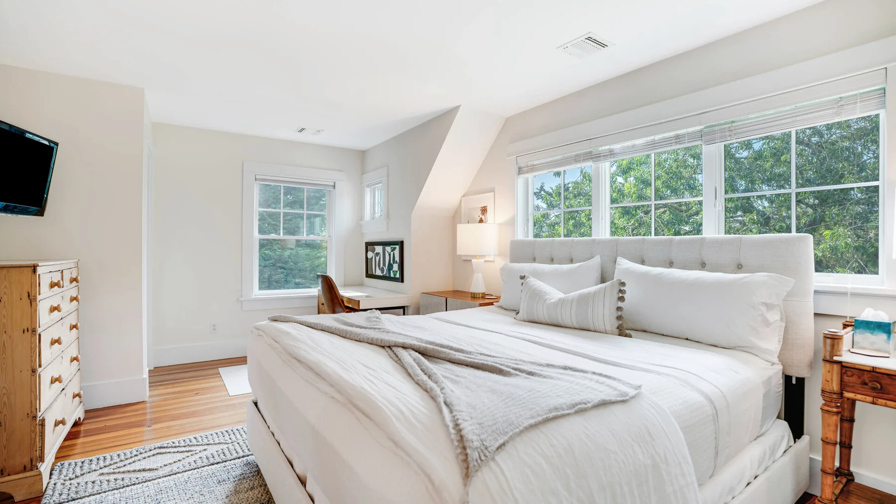 A bright bedroom with a large bed beneath wide windows.