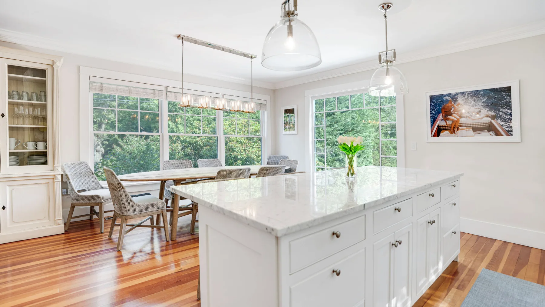 A bright kitchen with a large island, dining table, and windows overlooking greenery.