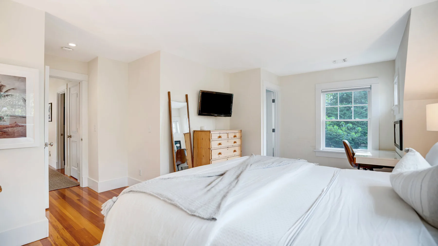 A bright bedroom with a neatly made bed, dresser, and window.