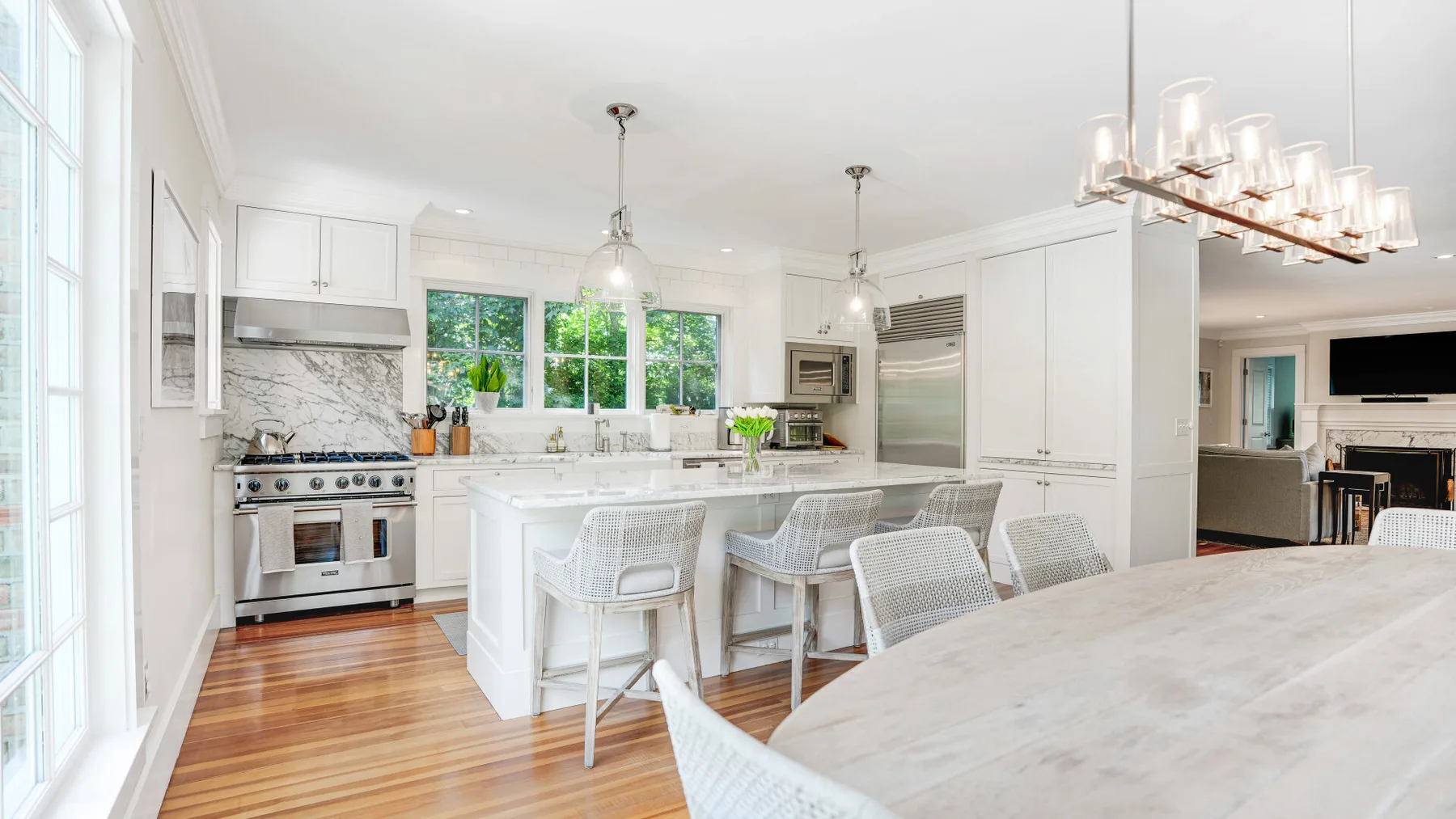 A bright white kitchen with a central island, seating, and large windows.