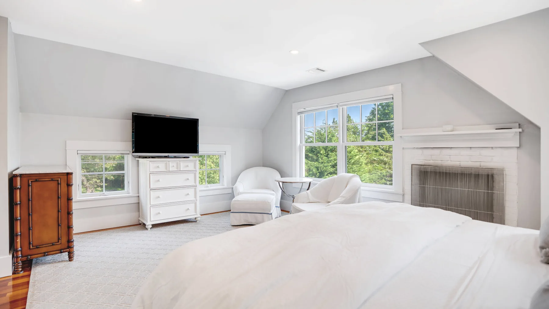 Bedroom with a large bed, seating, and a fireplace beside the windows.