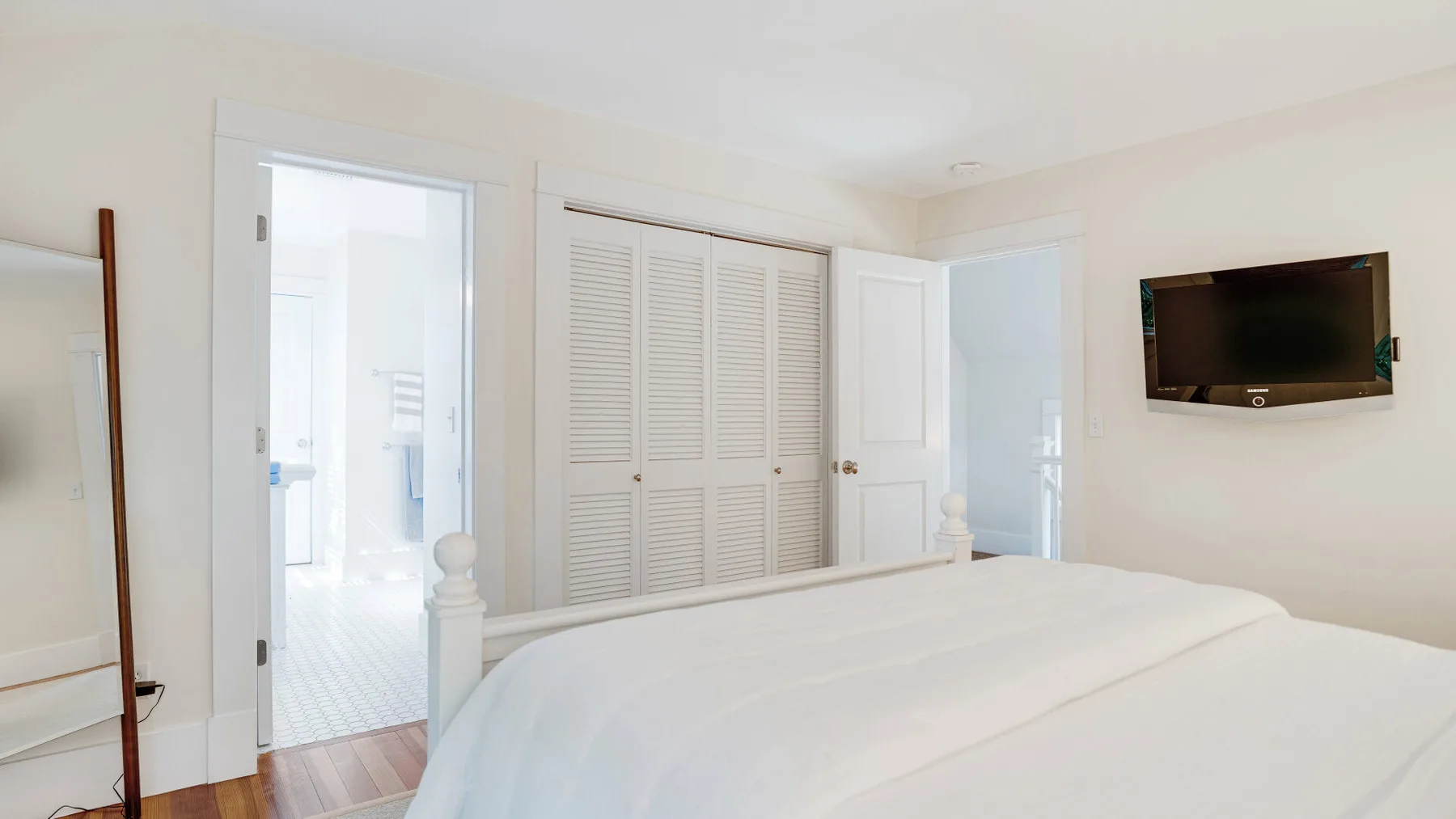 A bright bedroom with a white bed and a wall-mounted television.