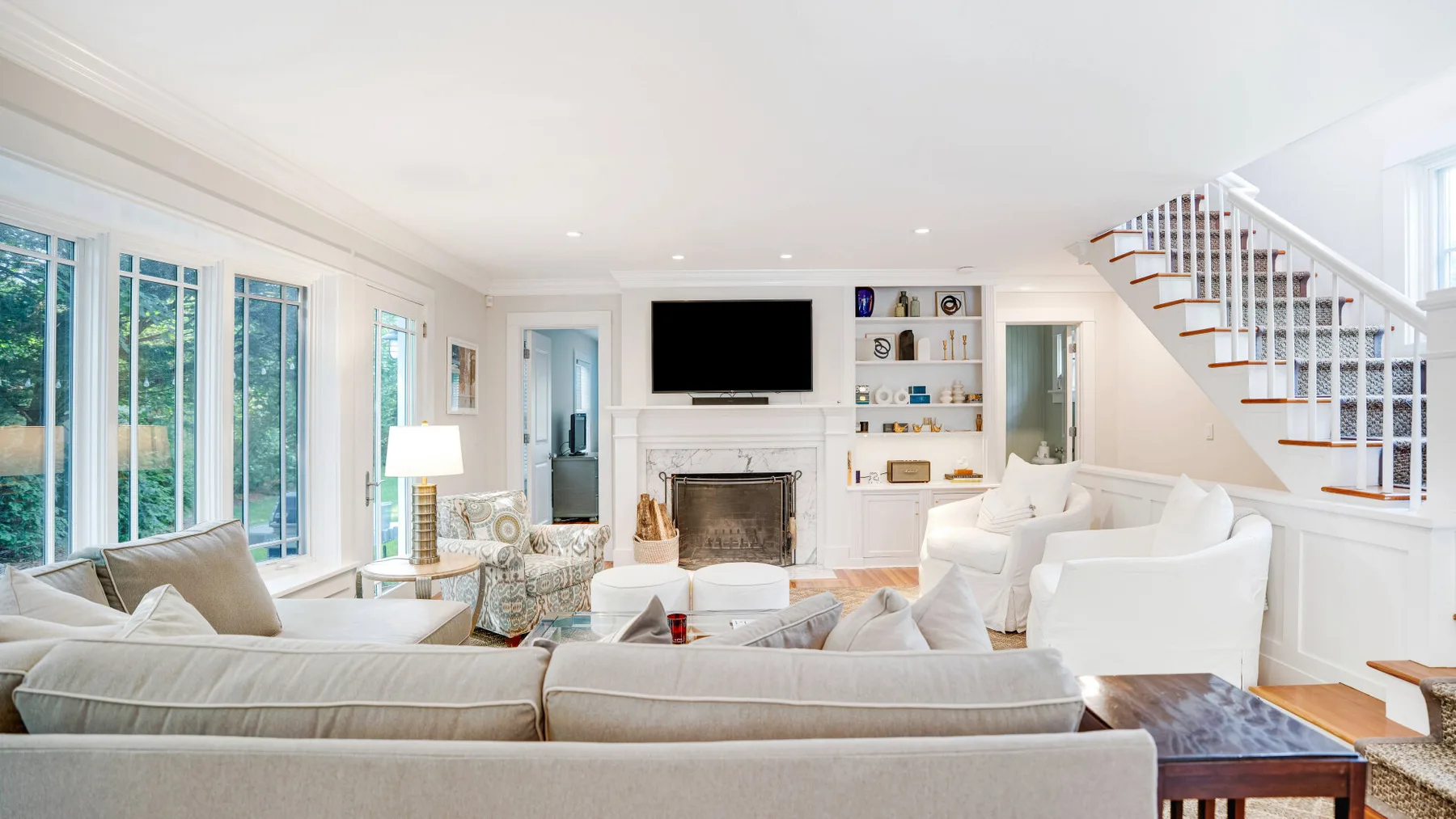 A bright living room with seating, large windows, and a staircase.