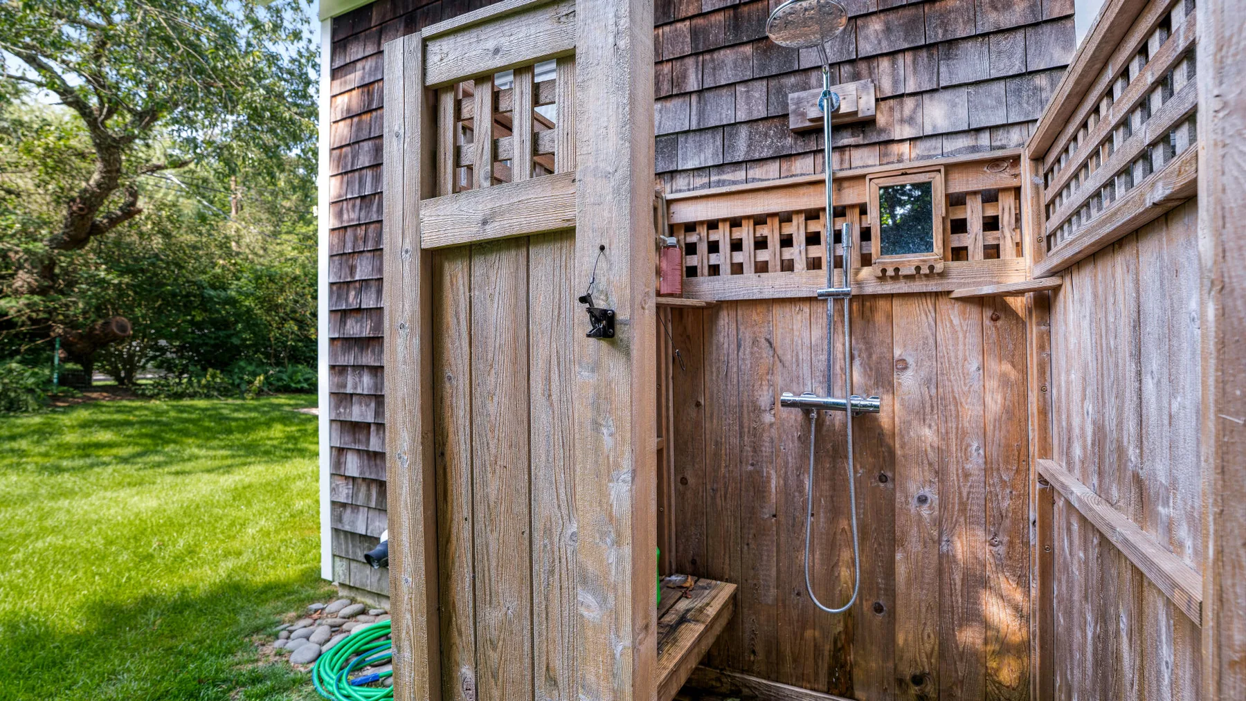 An outdoor shower area with a wooden privacy screen beside a grassy yard.