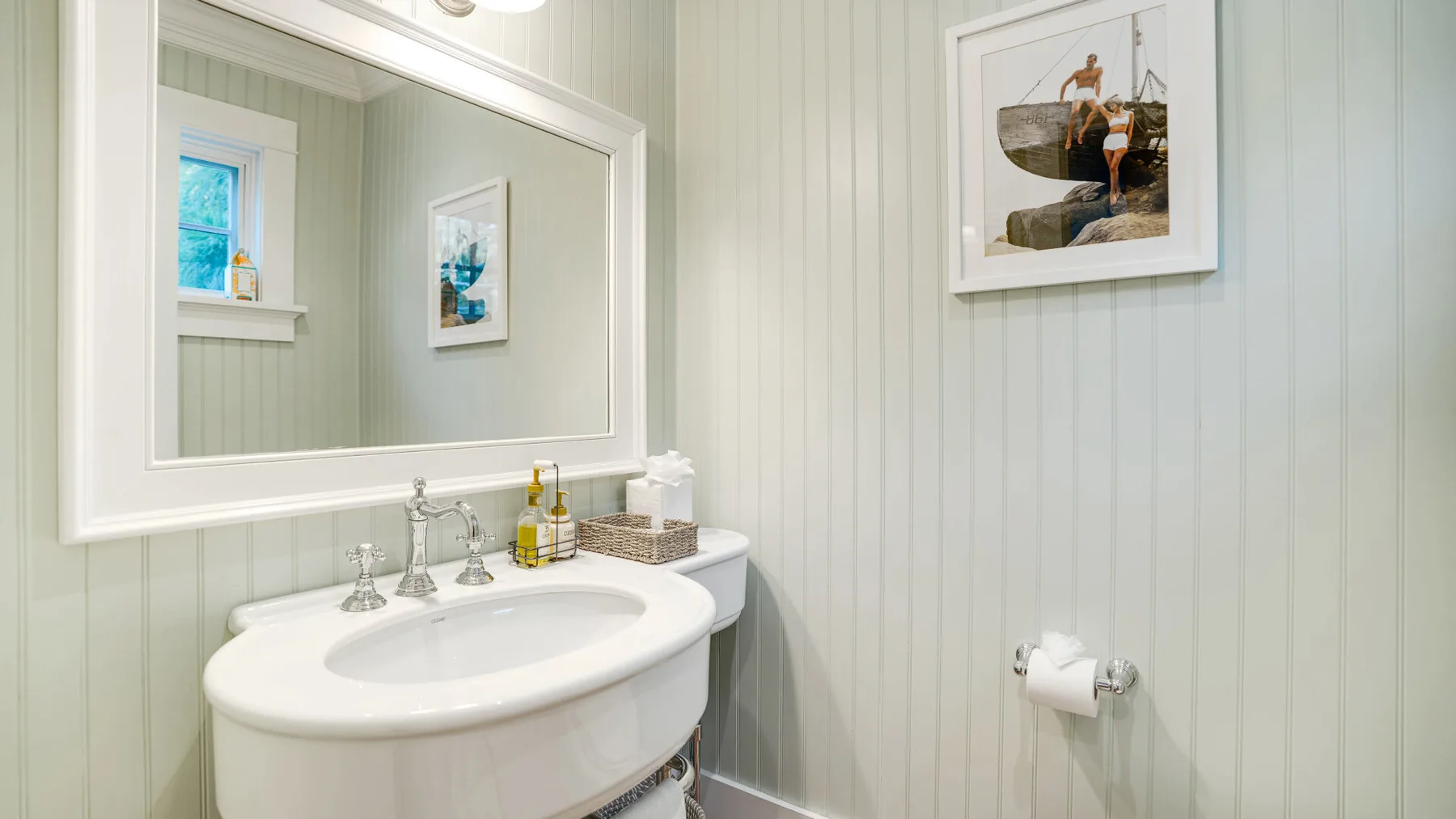 A bright bathroom with a large oval sink and framed wall art.