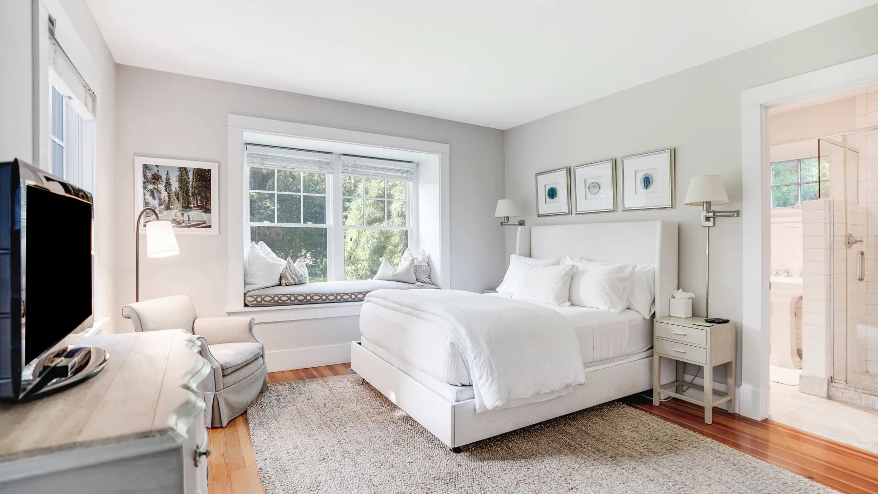 A bright bedroom with a white bed beneath a large window.