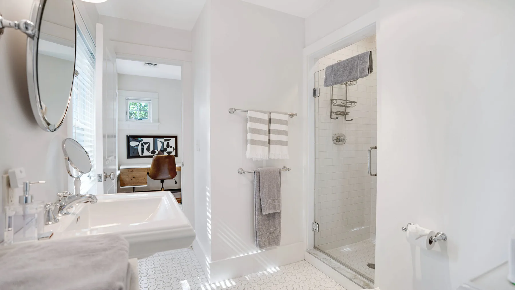 A bright bathroom with a sink, mirror, and glass shower beside a towel rack.