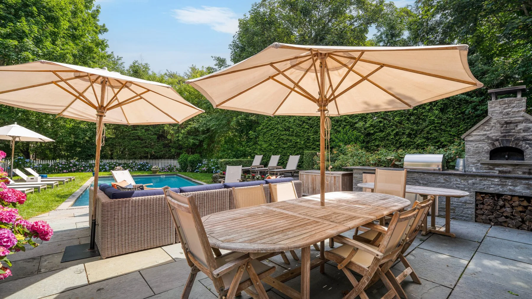 A patio dining area with a wooden table, umbrellas, and a swimming pool.