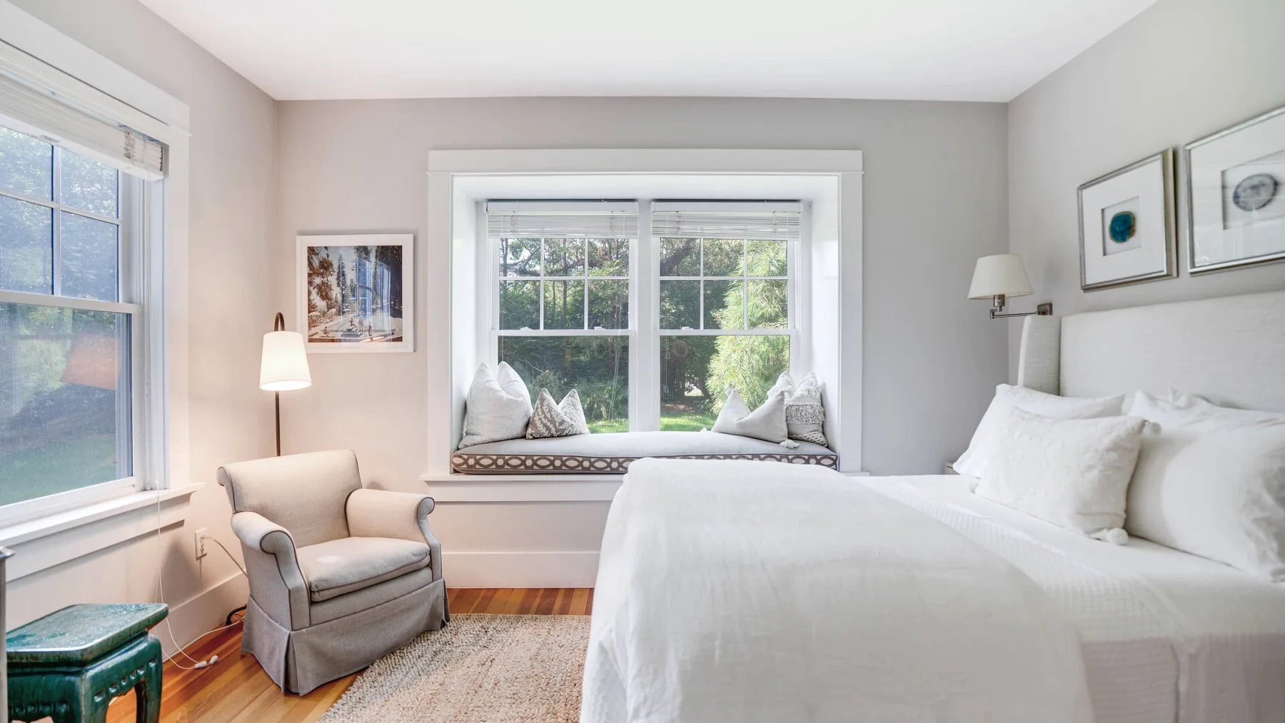 A bright bedroom with a large bed and a window seat overlooking greenery.